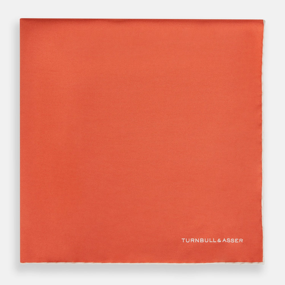 The Orange and White Piped Silk Pocket Square by Turnbull & Asser features a solid orange design with white piping and the brand’s logo in the bottom right corner, making it an elegant addition to any formal outfit.