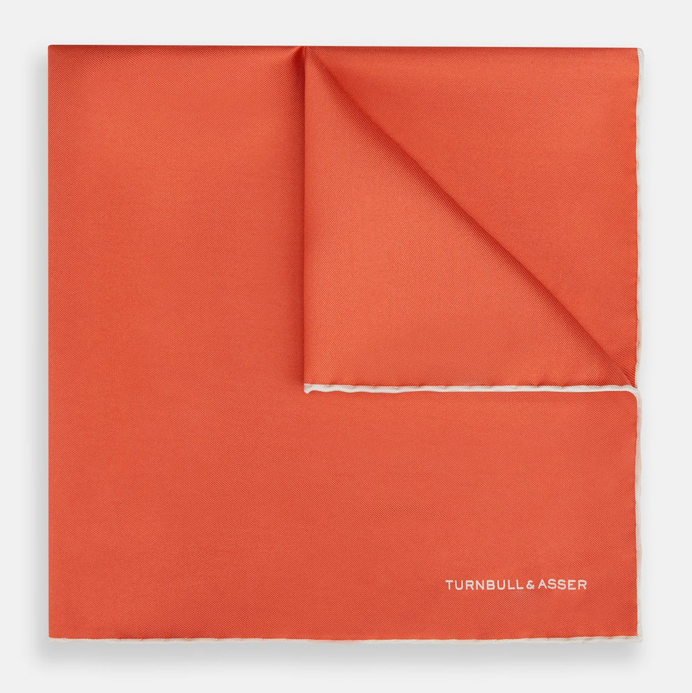 The Orange and White Piped Silk Pocket Square by Turnbull & Asser features a solid orange design with white piping and the brand’s logo in the bottom right corner, making it an elegant addition to any formal outfit.