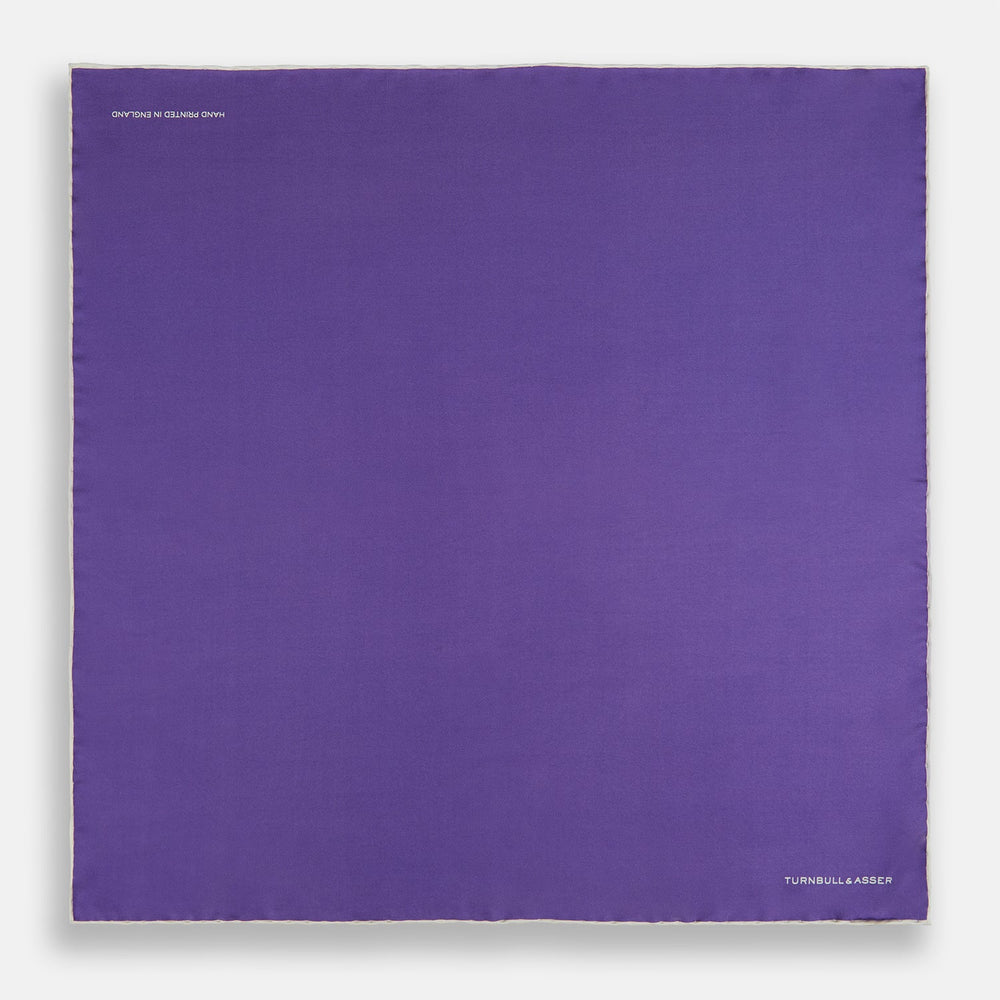 The Turnbull & Asser Violet and Ecru Piped Silk Pocket Square features a stitched edge and white brand logo, making it an elegant addition to formalwear.