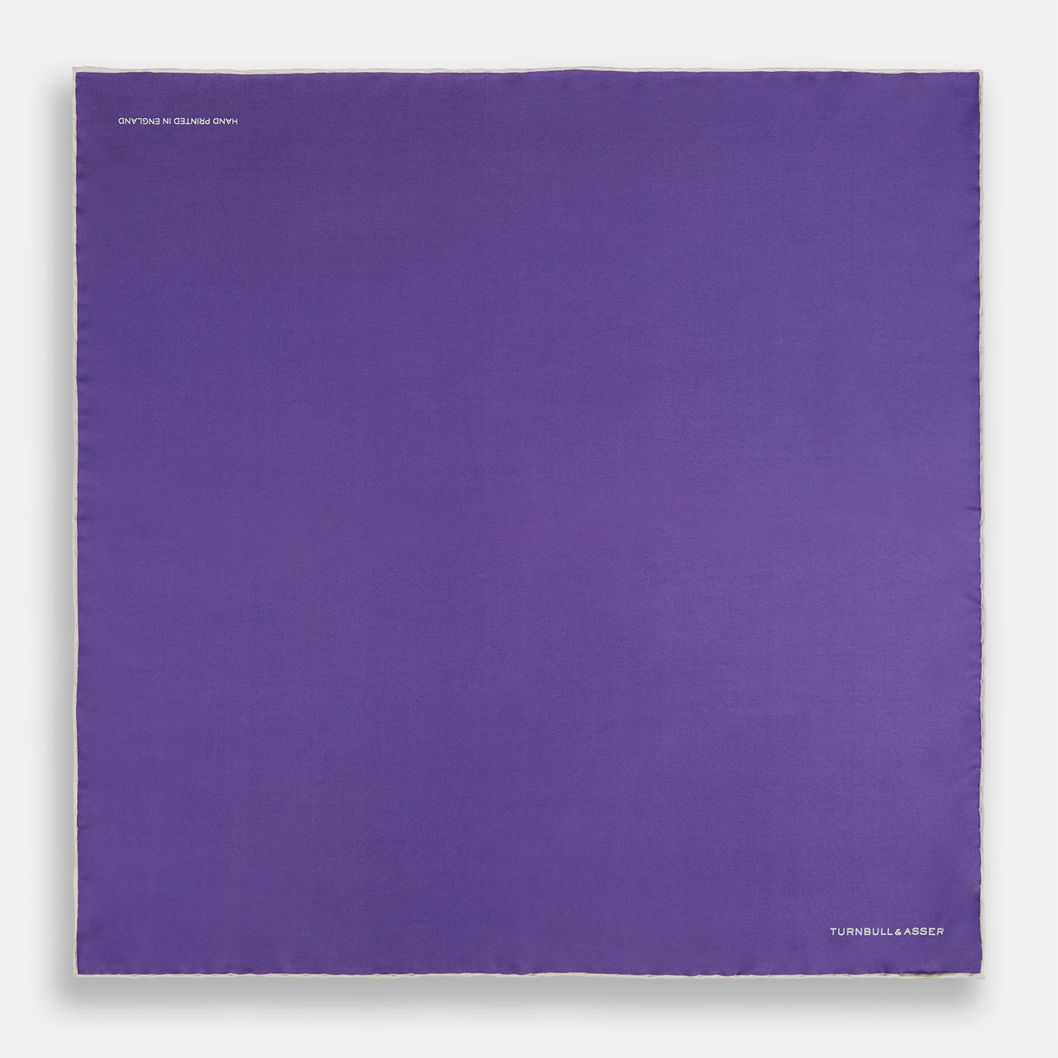 View 4 of product The Turnbull & Asser Violet and Ecru Piped Silk Pocket Square features a stitched edge and white brand logo, making it an elegant addition to formalwear.
