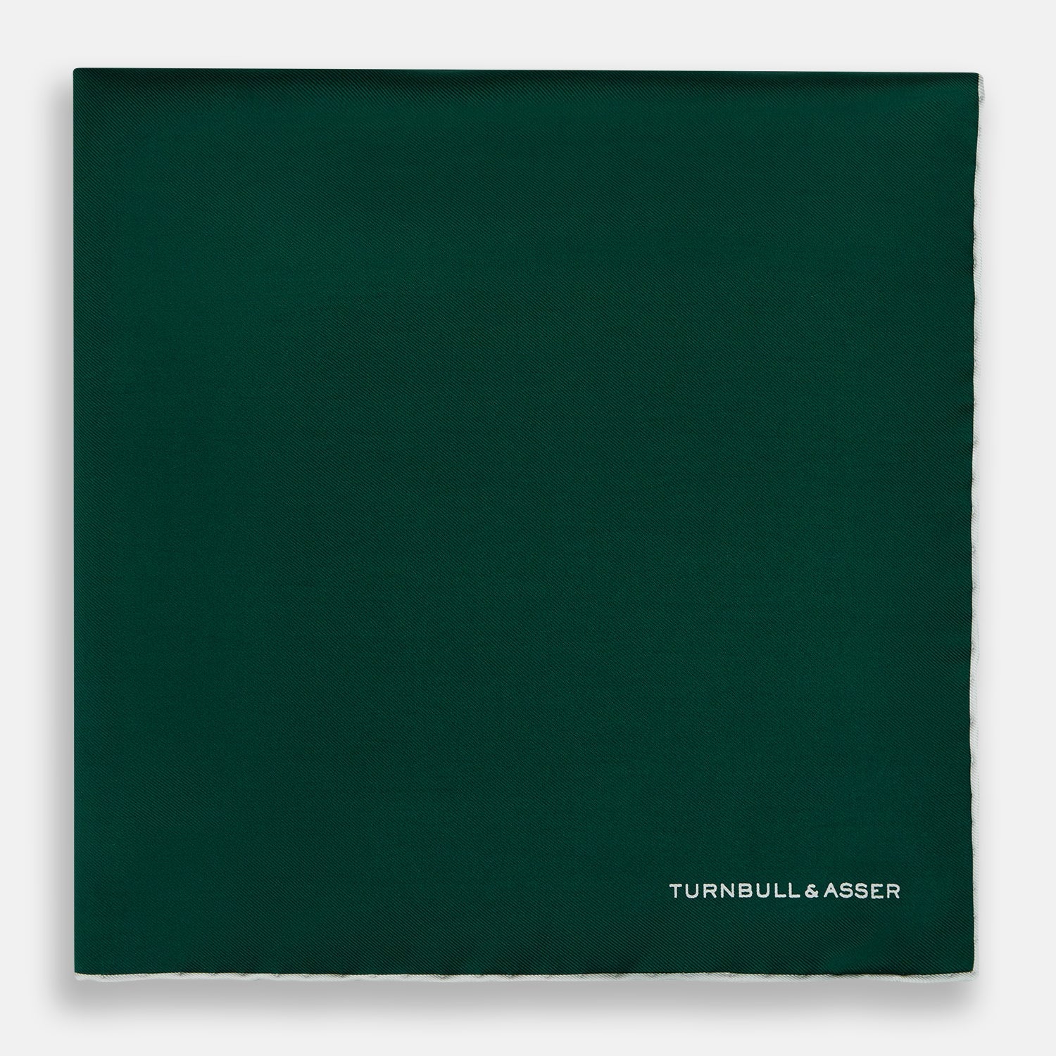 View 3 of product The FOREST GREEN AND ECRU PIPED SILK POCKET SQUARE by Turnbull & Asser features forest green silk with ecru piping, neatly folded to display both sides, and the brand name printed in white in the lower right corner—ideal for formal attire.