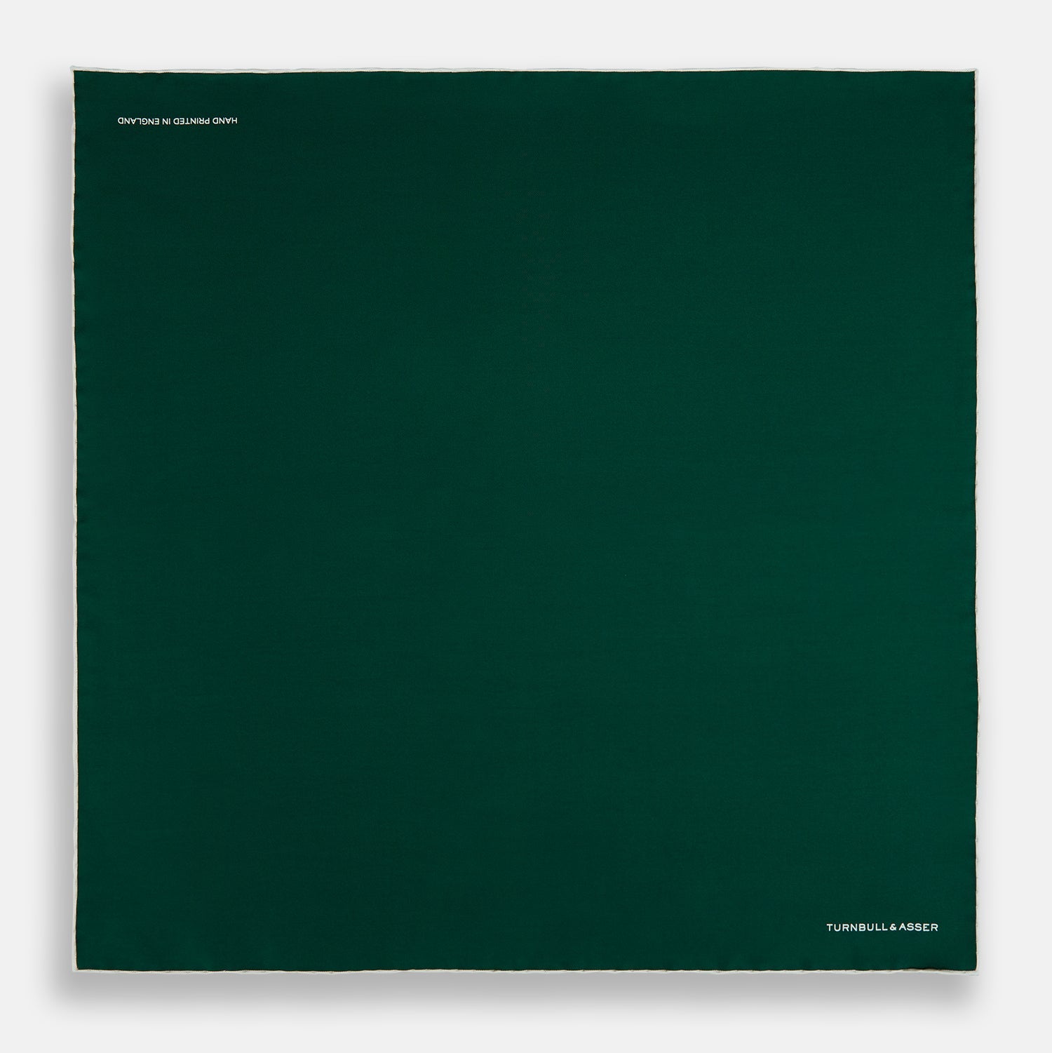 View 4 of product The FOREST GREEN AND ECRU PIPED SILK POCKET SQUARE by Turnbull & Asser features forest green silk with ecru piping, neatly folded to display both sides, and the brand name printed in white in the lower right corner—ideal for formal attire.