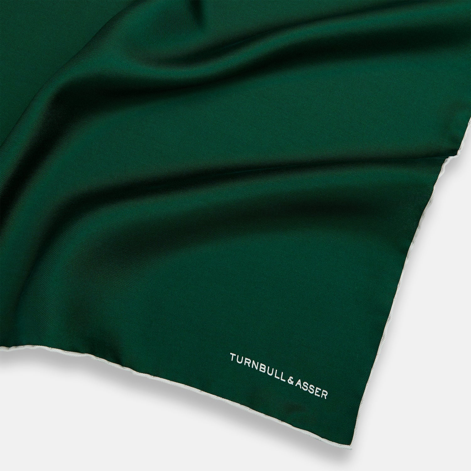 View 2 of product The FOREST GREEN AND ECRU PIPED SILK POCKET SQUARE by Turnbull & Asser features forest green silk with ecru piping, neatly folded to display both sides, and the brand name printed in white in the lower right corner—ideal for formal attire.