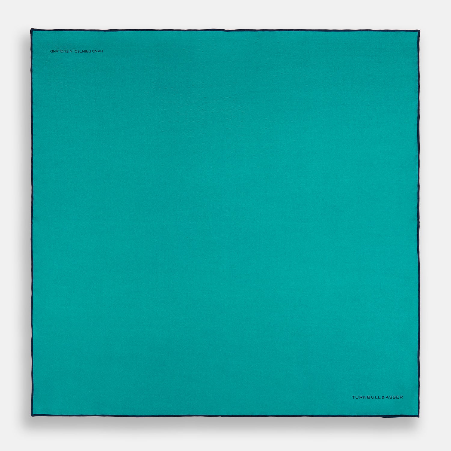 View 4 of product The Turquoise Piped Silk Pocket Square by Turnbull & Asser features dark blue edging and the brand’s logo, offering a sophisticated accent to formal outfits.