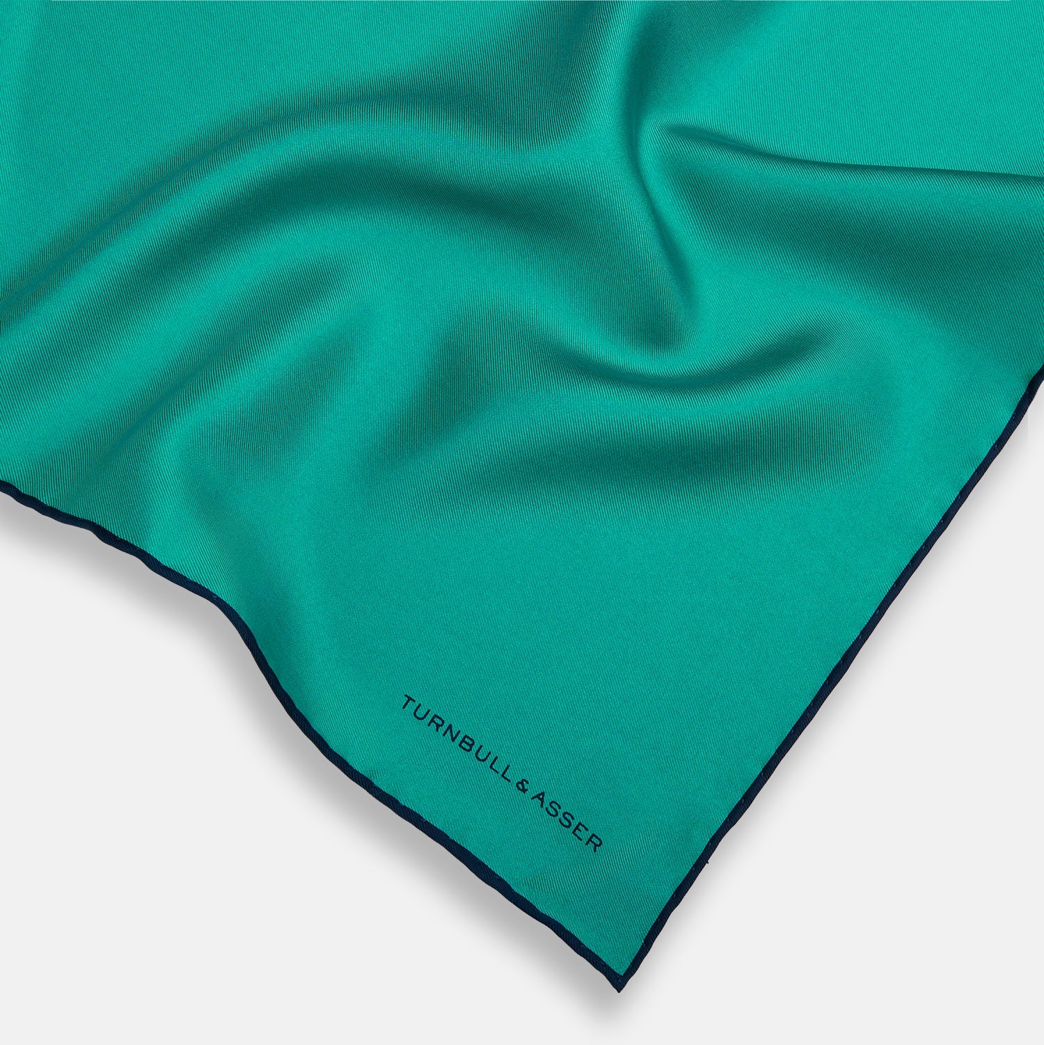 View 2 of product The Turquoise Piped Silk Pocket Square by Turnbull & Asser features dark blue edging and the brand’s logo, offering a sophisticated accent to formal outfits.