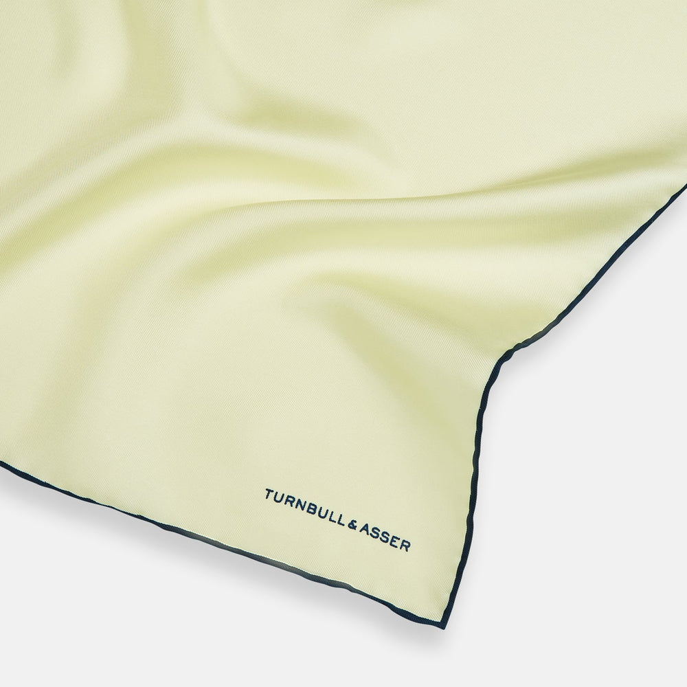 The Turnbull & Asser GOLD AND NAVY BLUE PIPED SILK POCKET SQUARE features navy piping and an embroidered logo—a refined accessory to elevate any formal look.