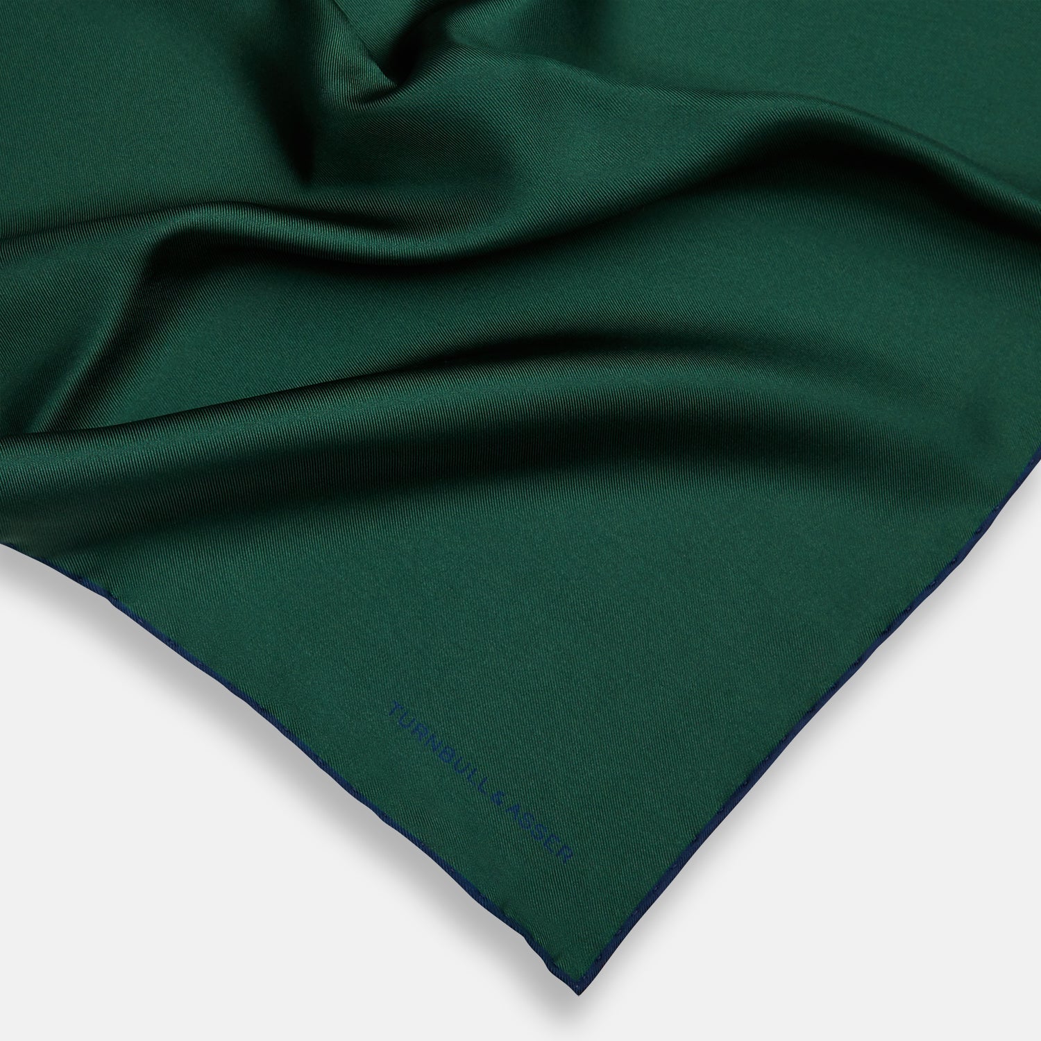 View 2 of product The Turnbull & Asser Petrol Green Piped Silk Pocket Square features a visible stitched edge and a discreet blue logo on the turned-down corner, adding an elegant accent to formal attire.