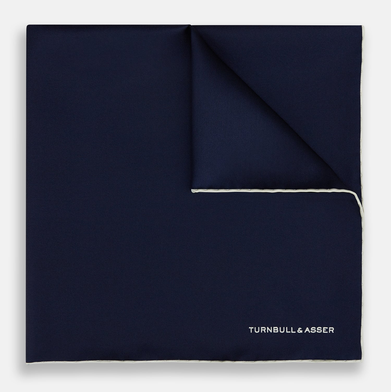 View 1 of product The Dark Blue Piped Silk Pocket Square by Turnbull & Asser features white piping, a one-corner fold revealing the underside, and the brand's name embroidered in white—perfect for formal occasions.