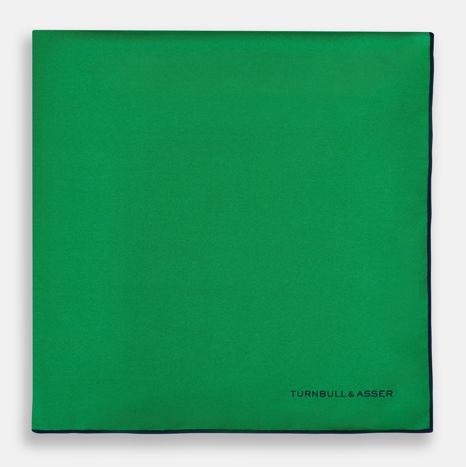 View 3 of product The Green Piped Silk Pocket Square by Turnbull & Asser features dark blue stitched edges and a neat fold—ideal for formal occasions. The Turnbull & Asser name is printed in black on the lower right corner.