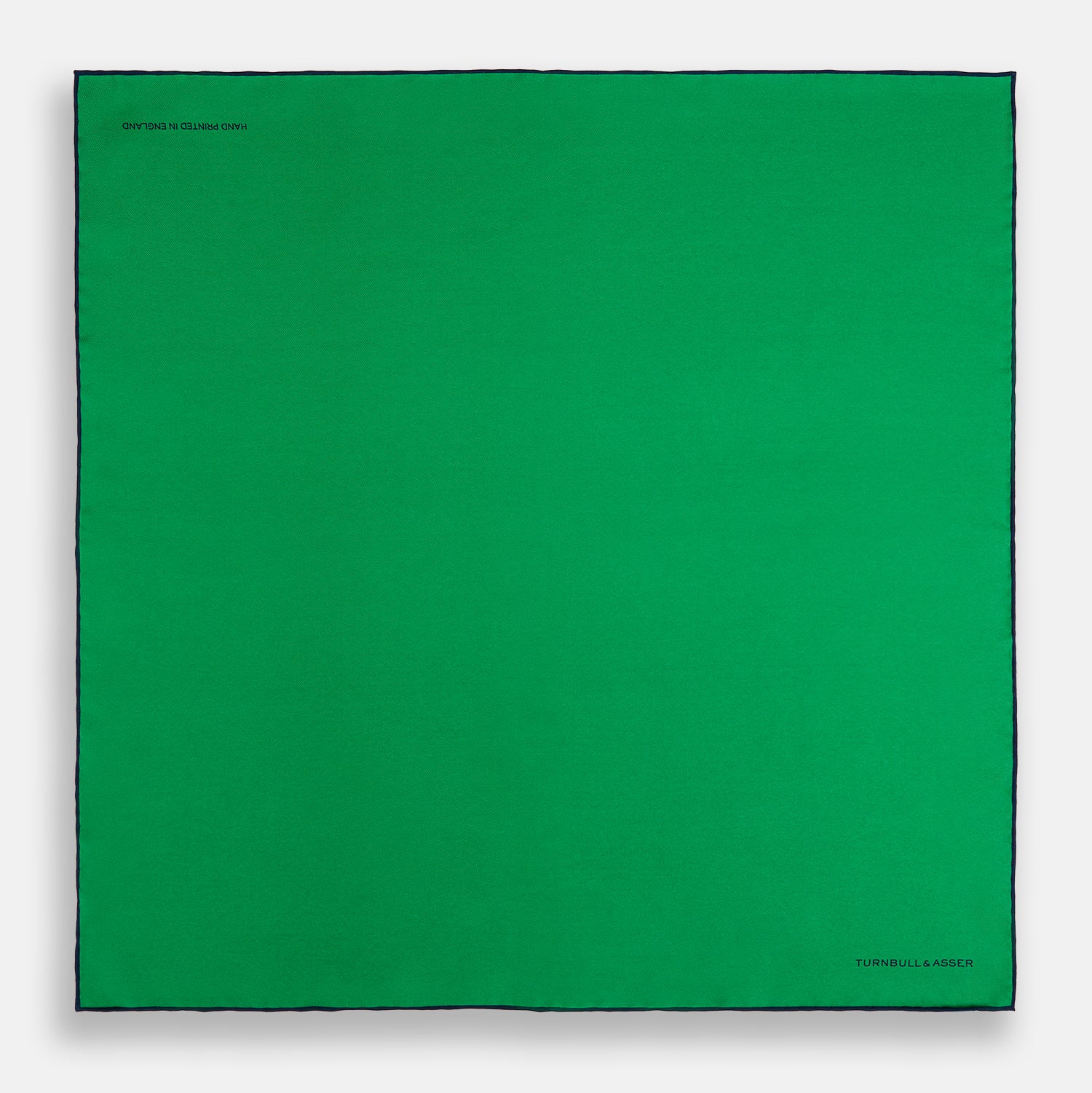 View 4 of product The Green Piped Silk Pocket Square by Turnbull & Asser features dark blue stitched edges and a neat fold—ideal for formal occasions. The Turnbull & Asser name is printed in black on the lower right corner.