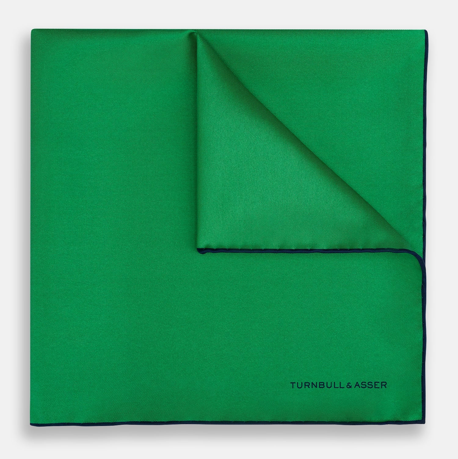 View 1 of product The Green Piped Silk Pocket Square by Turnbull & Asser features dark blue stitched edges and a neat fold—ideal for formal occasions. The Turnbull & Asser name is printed in black on the lower right corner.
