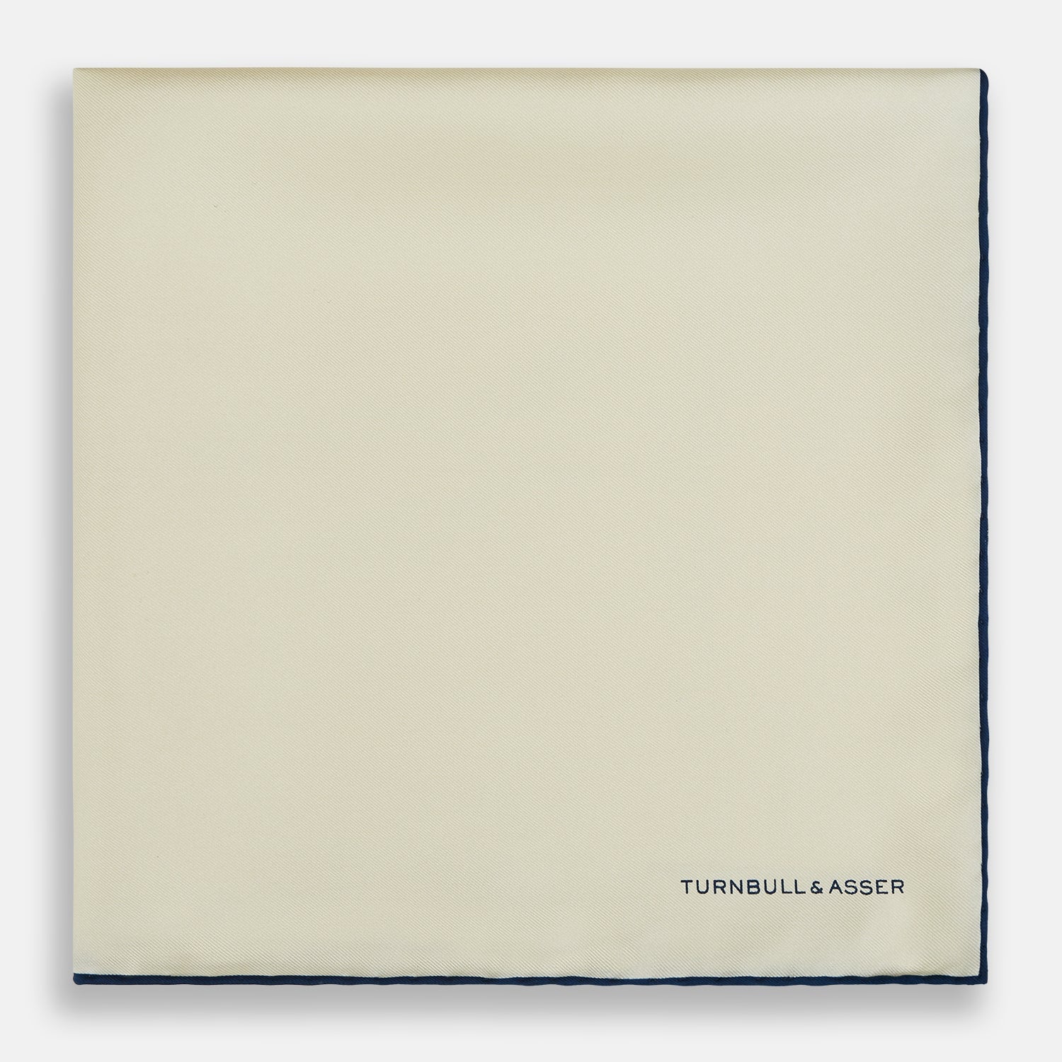 View 3 of product The Ecru and Navy Blue Piped Silk Pocket Square by Turnbull & Asser features contrasting navy piping and finely embroidered branding—an elegant finishing touch to any formal look.