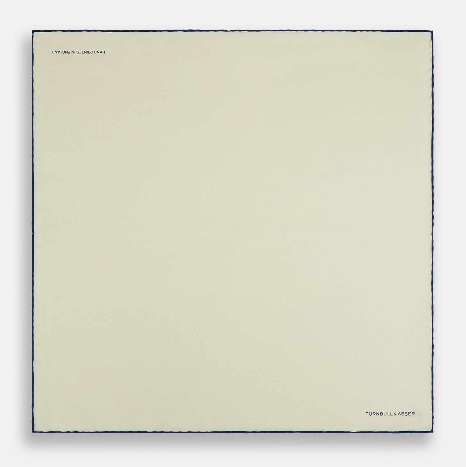 View 4 of product The Ecru and Navy Blue Piped Silk Pocket Square by Turnbull & Asser features contrasting navy piping and finely embroidered branding—an elegant finishing touch to any formal look.