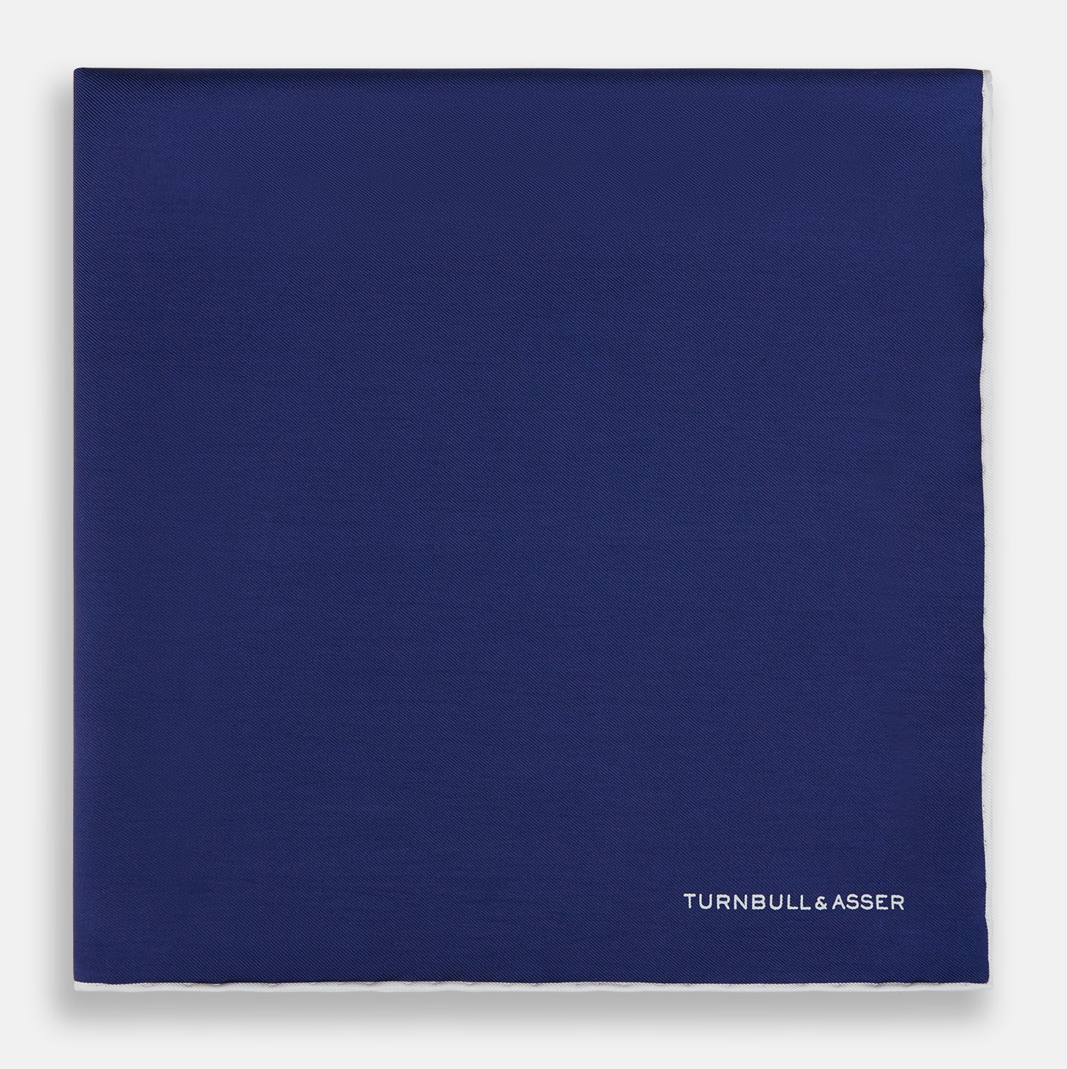 View 3 of product The Turnbull & Asser Mid Blue Piped Silk Pocket Square features a mid-blue hue with white edging, ideal for formal wear, and is finished with the brand’s name printed in white on the bottom right corner.
