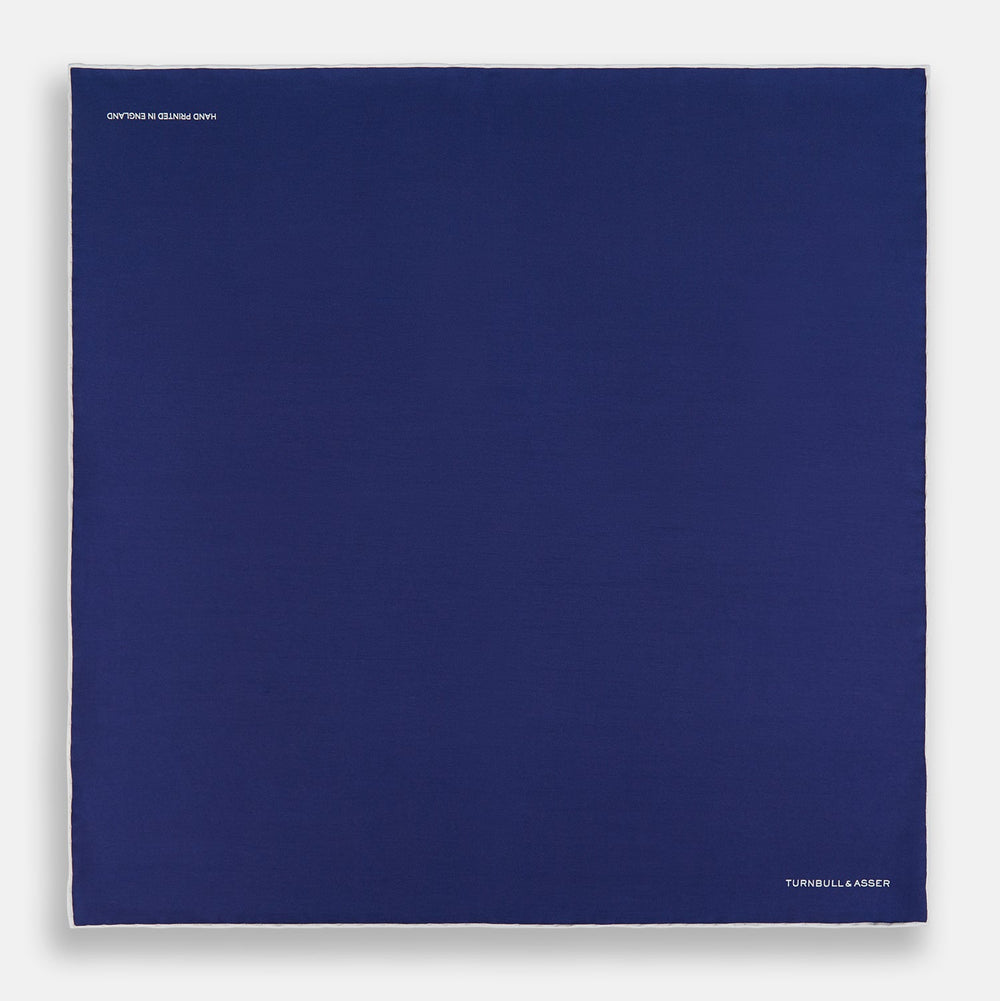 The Turnbull & Asser Mid Blue Piped Silk Pocket Square features a mid-blue hue with white edging, ideal for formal wear, and is finished with the brand’s name printed in white on the bottom right corner.