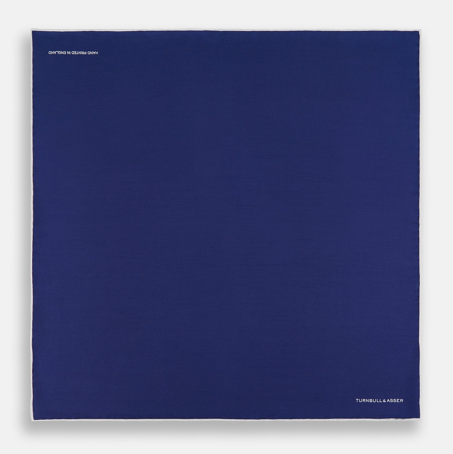 View 4 of product The Turnbull & Asser Mid Blue Piped Silk Pocket Square features a mid-blue hue with white edging, ideal for formal wear, and is finished with the brand’s name printed in white on the bottom right corner.