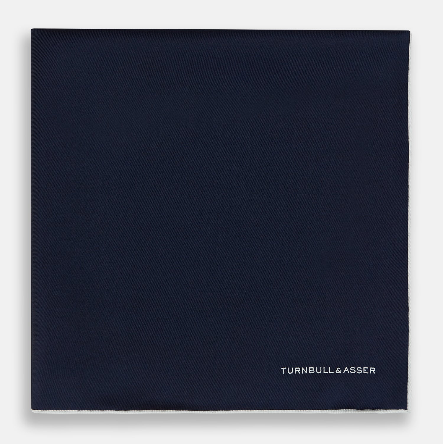 View 3 of product The Midnight Blue Piped Silk Pocket Square from Turnbull & Asser features crisp white trim and subtle branding, making it the ideal accessory to elevate your formal look.