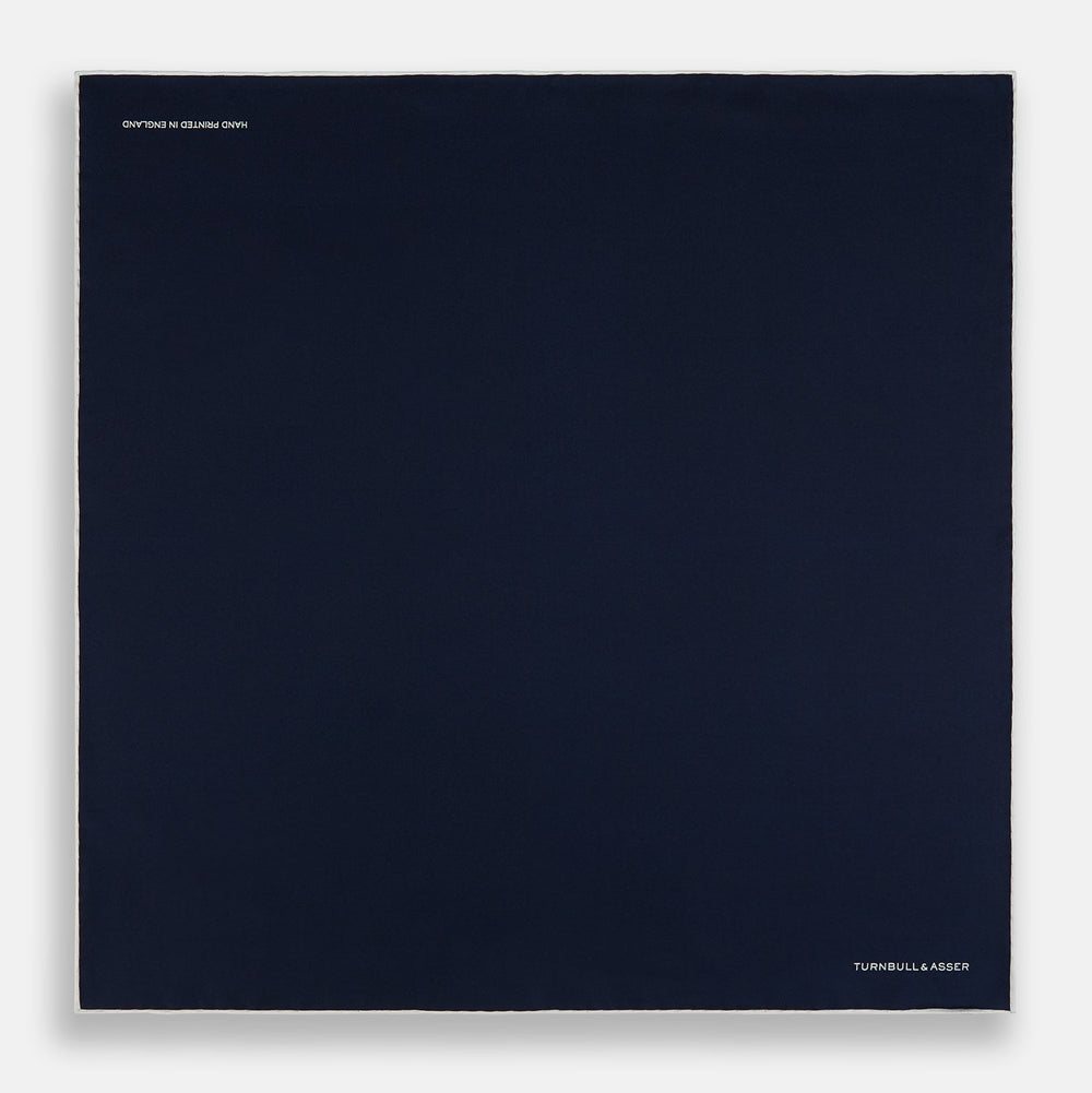 The Midnight Blue Piped Silk Pocket Square from Turnbull & Asser features crisp white trim and subtle branding, making it the ideal accessory to elevate your formal look.