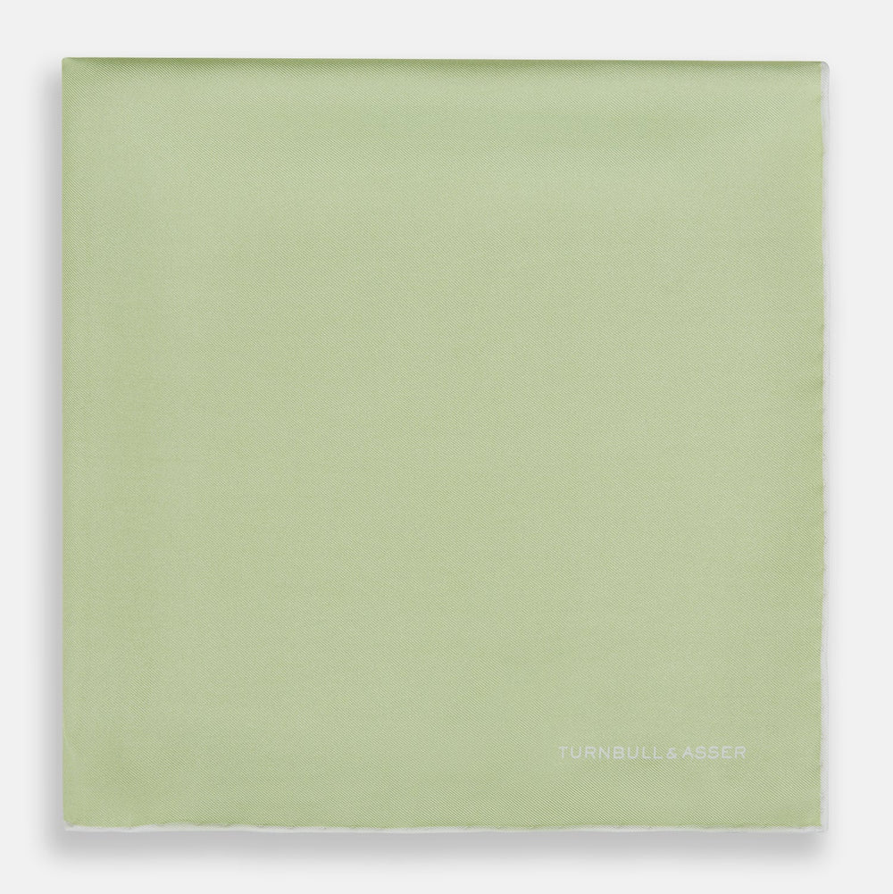 The Turnbull & Asser Mint and Ecru Piped Silk Pocket Square features a mint green silk fabric with subtle sheen and ecru piping, perfect for formal attire. "Turnbull & Asser" is embroidered in white in one corner.