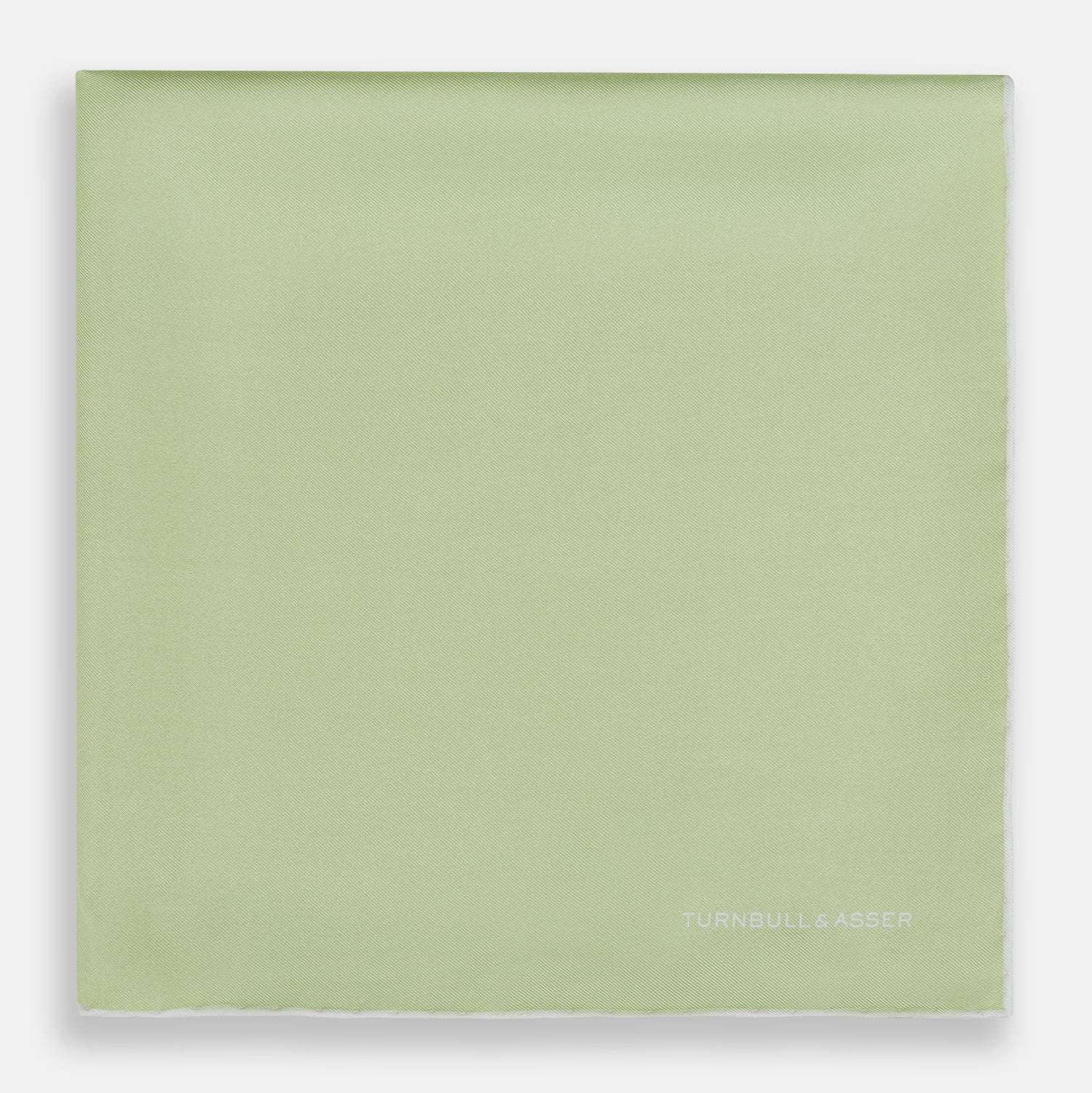 View 3 of product The Turnbull & Asser Mint and Ecru Piped Silk Pocket Square features a mint green silk fabric with subtle sheen and ecru piping, perfect for formal attire. "Turnbull & Asser" is embroidered in white in one corner.