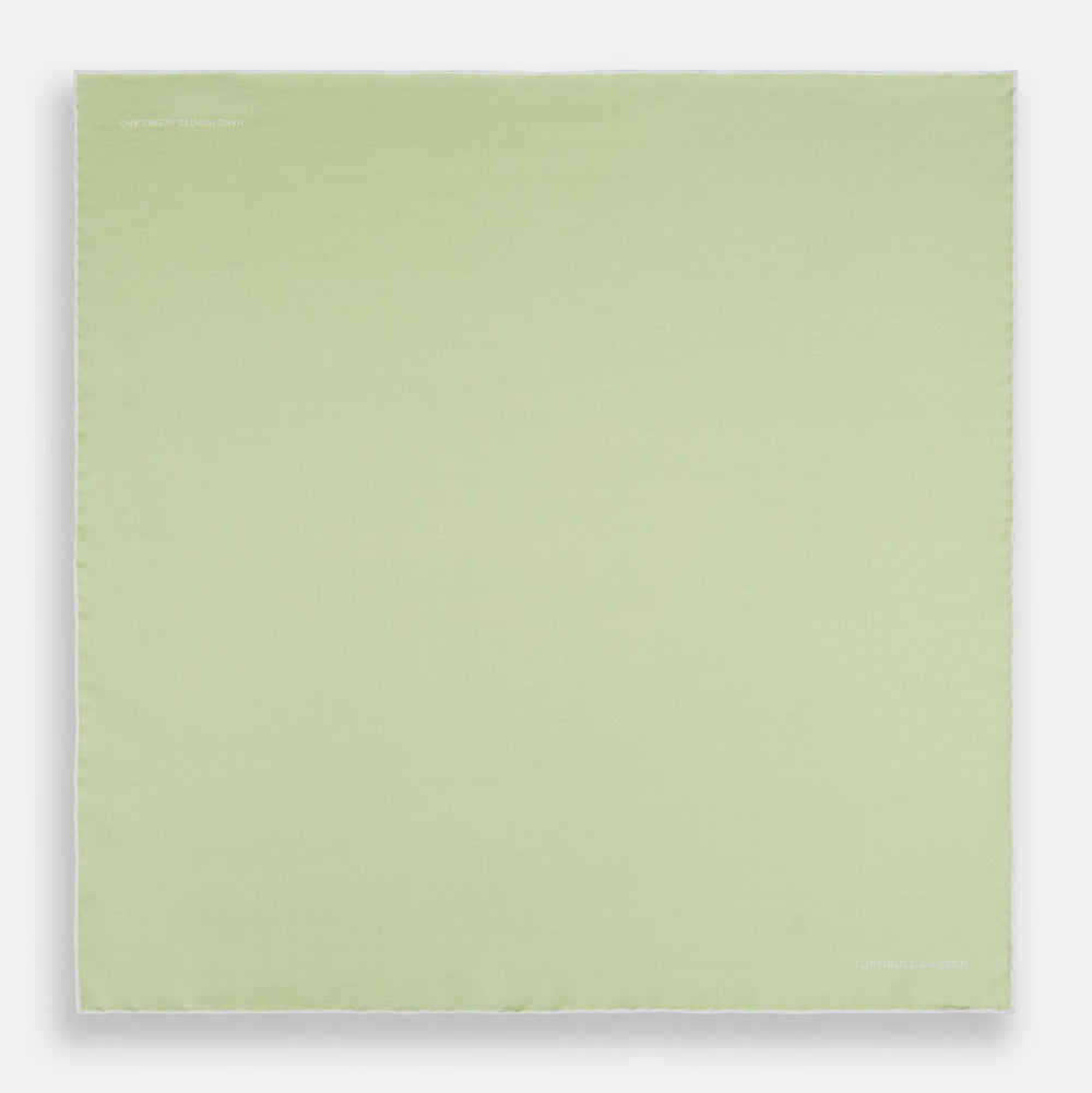 The Turnbull & Asser Mint and Ecru Piped Silk Pocket Square features a mint green silk fabric with subtle sheen and ecru piping, perfect for formal attire. "Turnbull & Asser" is embroidered in white in one corner.