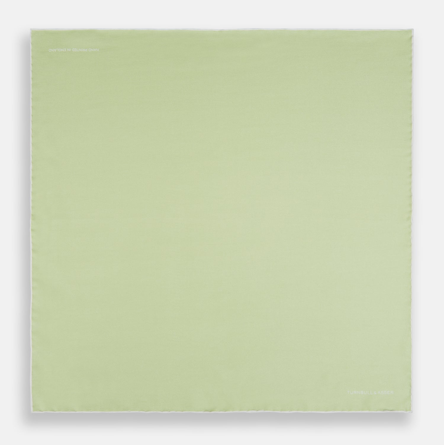 View 4 of product The Turnbull & Asser Mint and Ecru Piped Silk Pocket Square features a mint green silk fabric with subtle sheen and ecru piping, perfect for formal attire. "Turnbull & Asser" is embroidered in white in one corner.