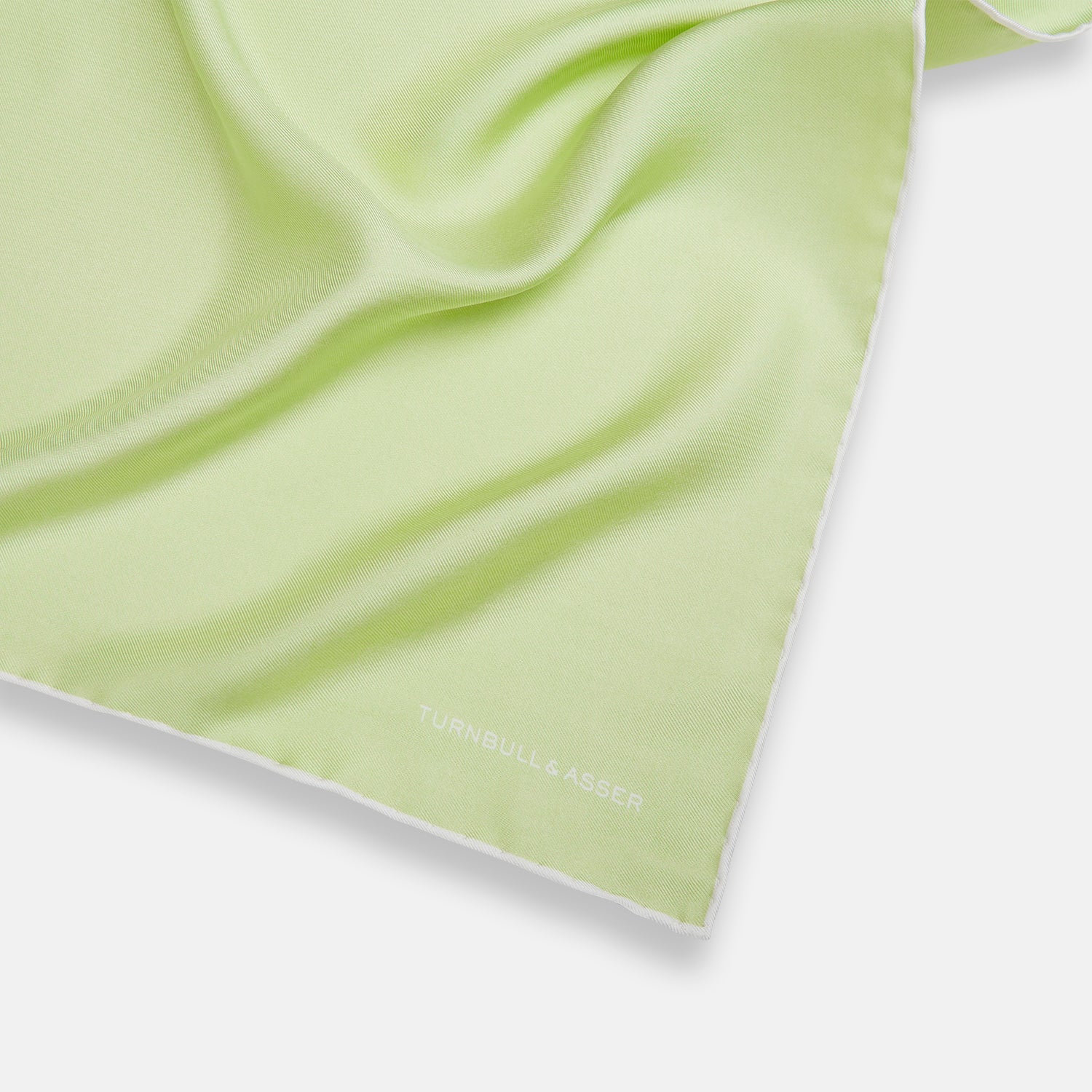 View 2 of product The Turnbull & Asser Mint and Ecru Piped Silk Pocket Square features a mint green silk fabric with subtle sheen and ecru piping, perfect for formal attire. "Turnbull & Asser" is embroidered in white in one corner.