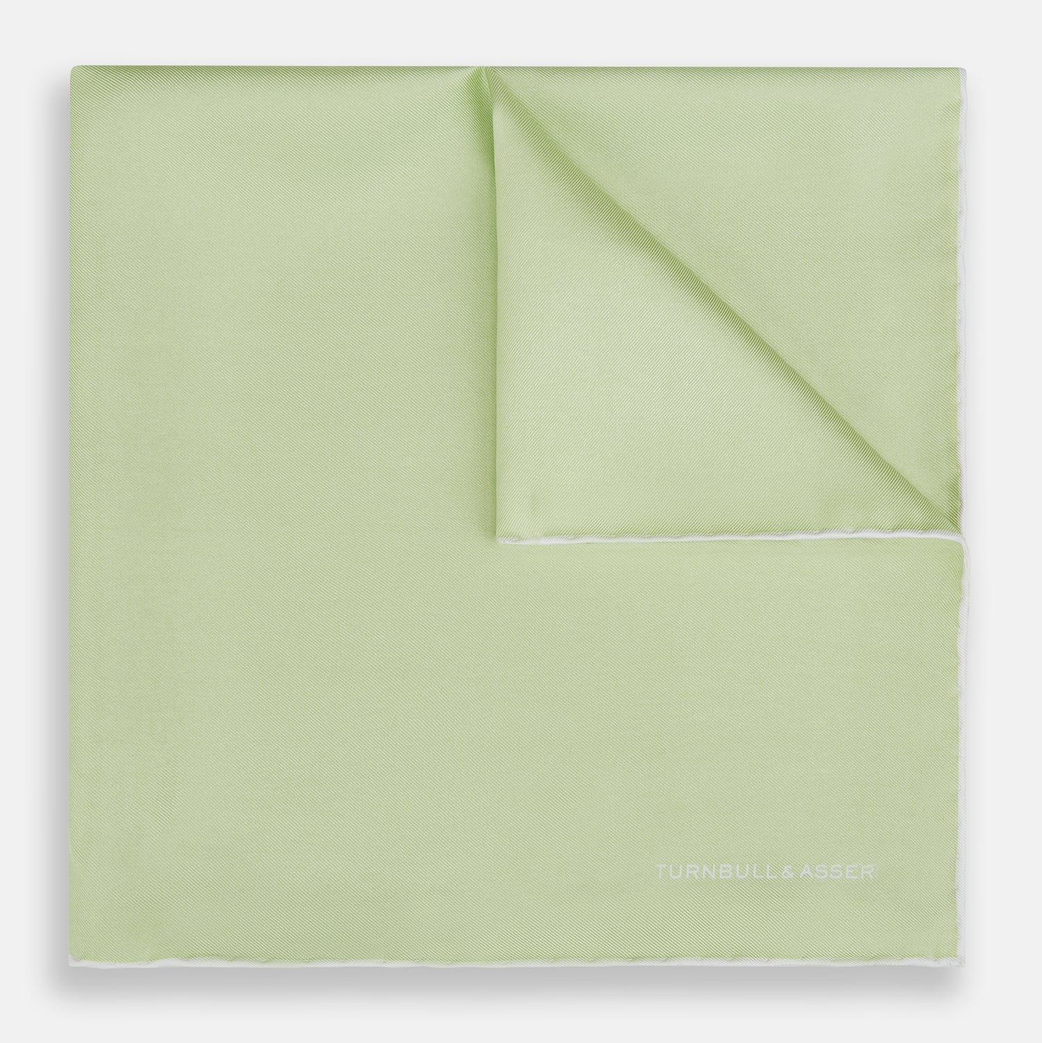 View 1 of product The Turnbull & Asser Mint and Ecru Piped Silk Pocket Square features a mint green silk fabric with subtle sheen and ecru piping, perfect for formal attire. "Turnbull & Asser" is embroidered in white in one corner.