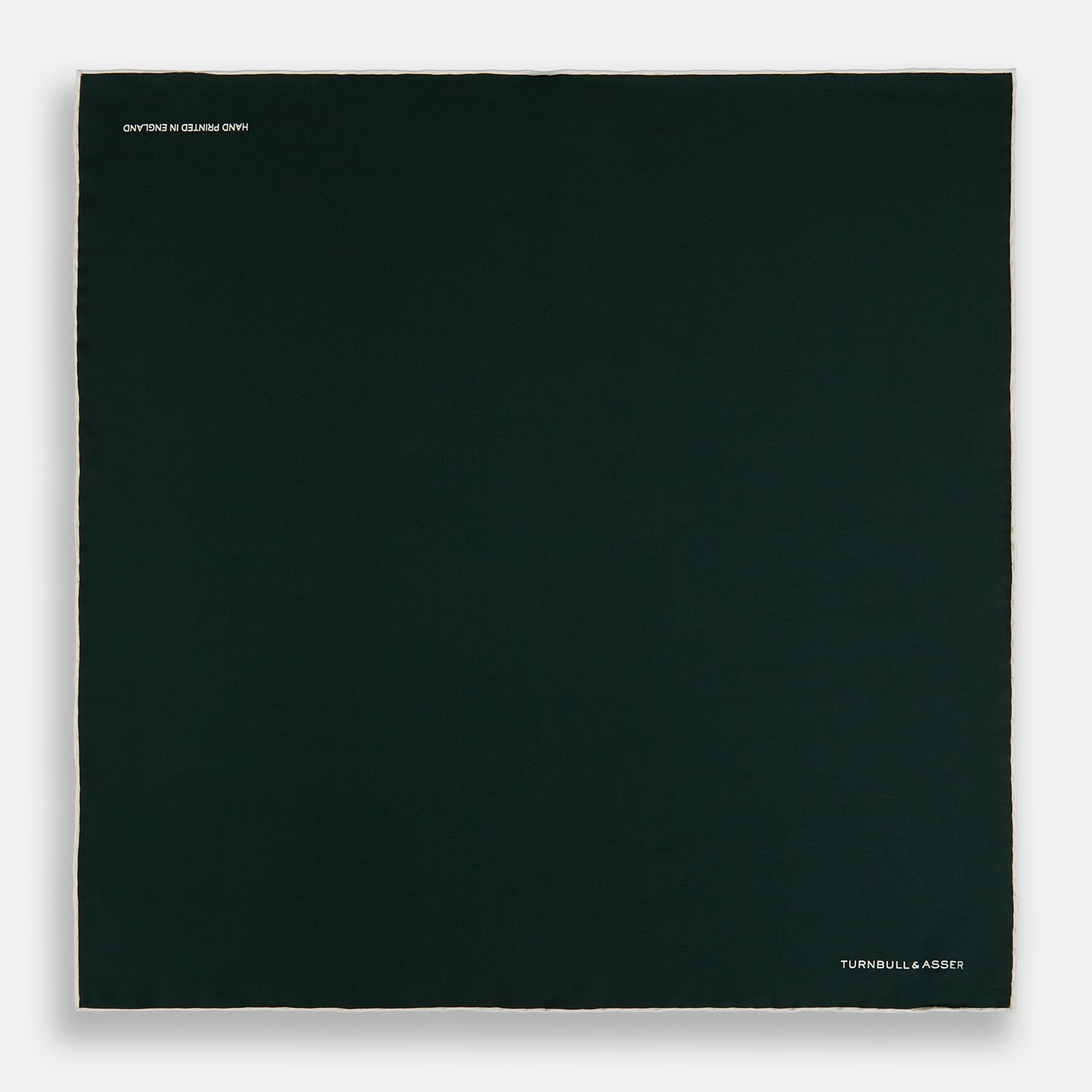 View 4 of product The DARK GREEN AND ECRU PIPED SILK POCKET SQUARE by Turnbull & Asser features ecru edging and the brand's logo in one corner, making it a refined choice for formal attire. One corner is folded to show the reverse side.