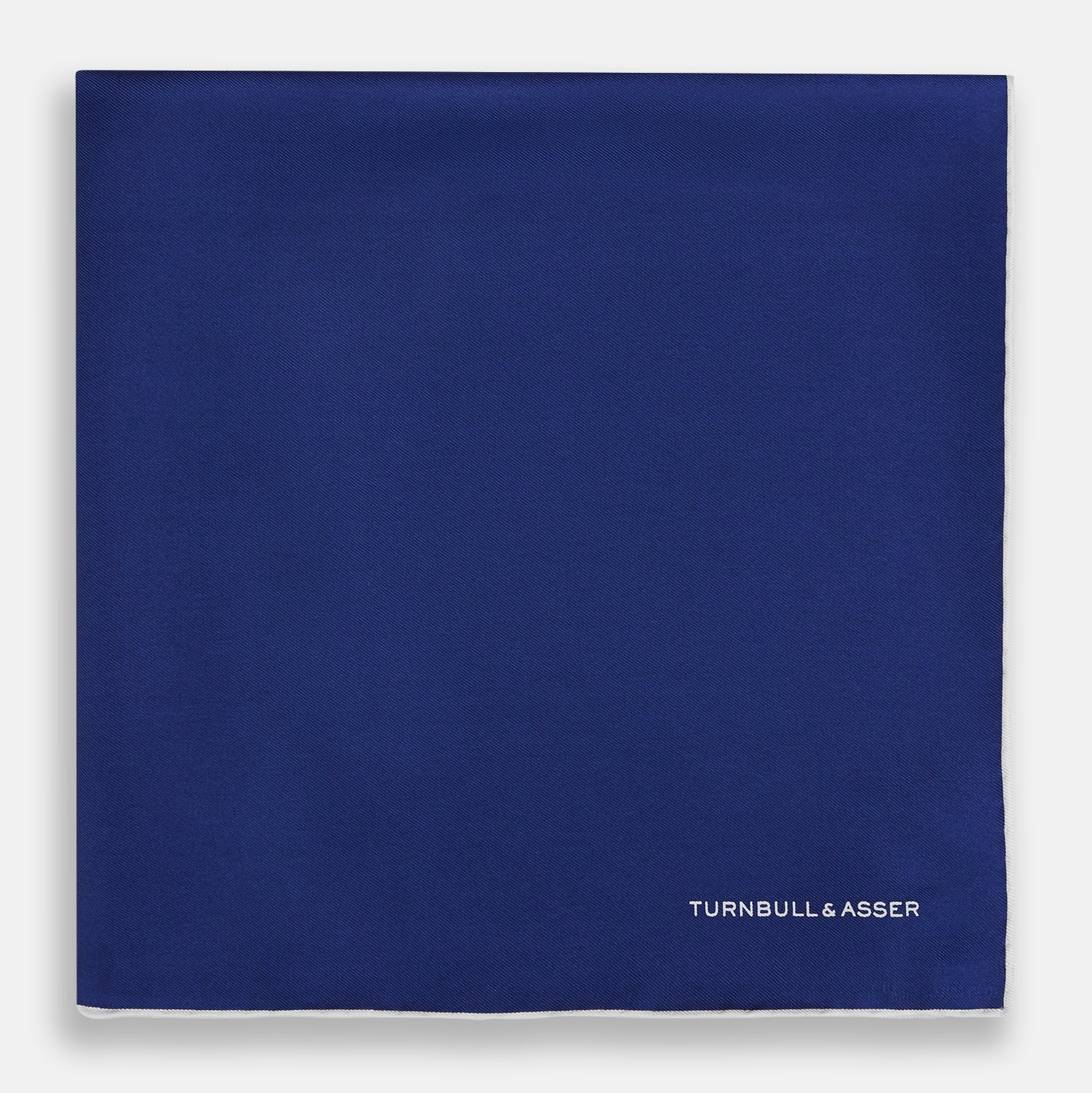 View 3 of product The Turnbull & Asser Royal Blue Piped Silk Pocket Square features white piping and the brand logo embroidered in white at the bottom right, making it perfect for formalwear.