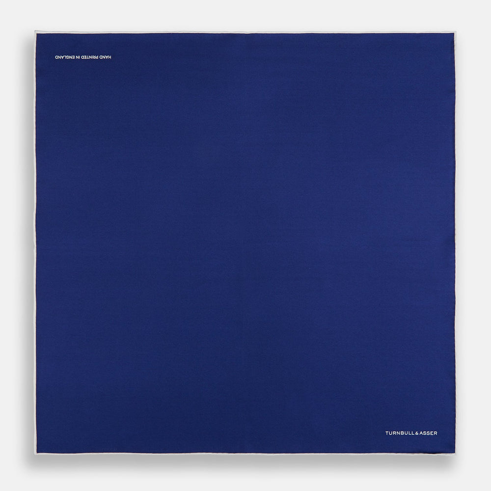 The Turnbull & Asser Royal Blue Piped Silk Pocket Square features white piping and the brand logo embroidered in white at the bottom right, making it perfect for formalwear.