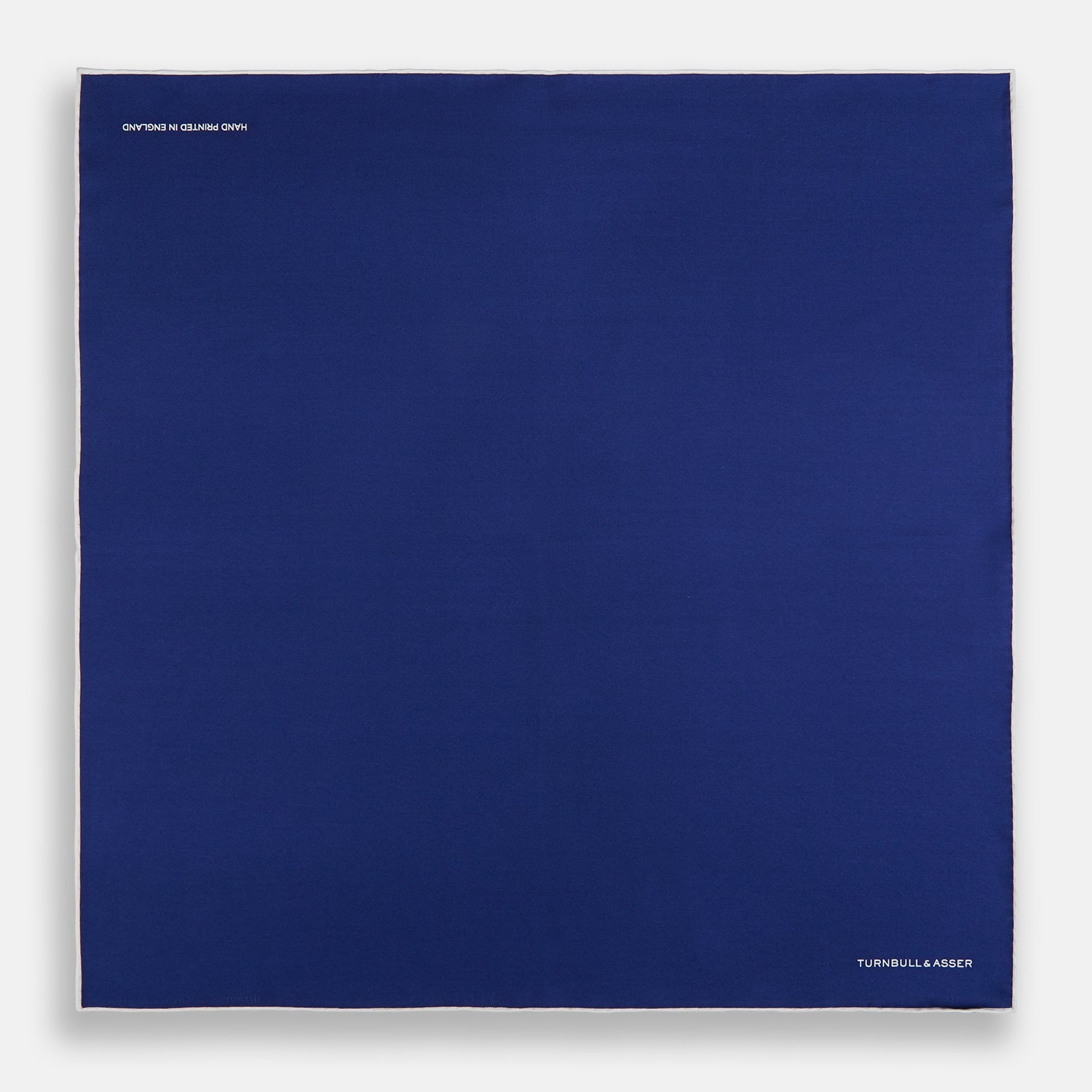 View 4 of product The Turnbull & Asser Royal Blue Piped Silk Pocket Square features white piping and the brand logo embroidered in white at the bottom right, making it perfect for formalwear.