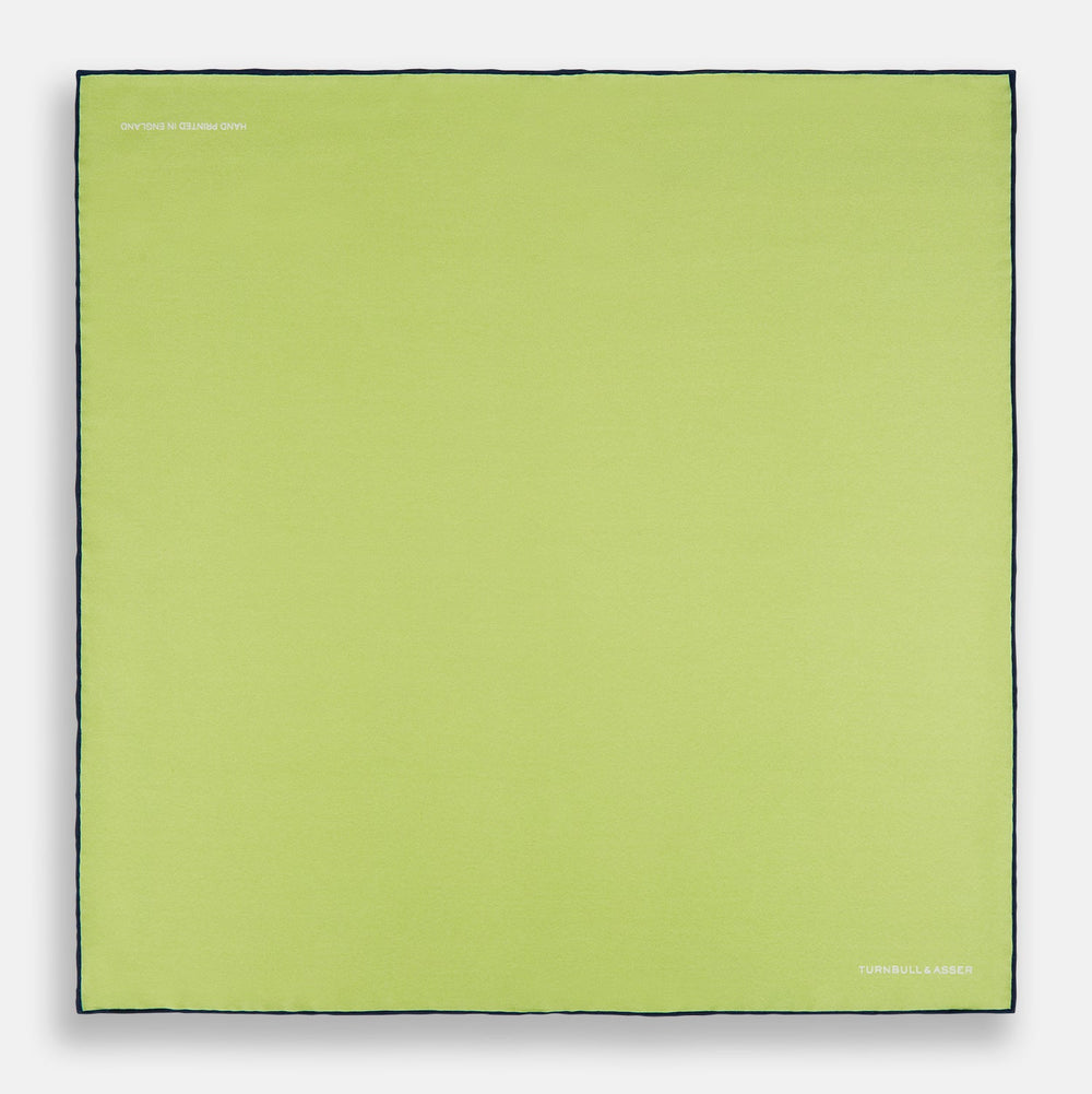 The Pistachio Green and Navy Piped Silk Pocket Square by Turnbull & Asser features crisp navy edging and an elegant brand logo, making it a refined addition to any formal outfit.