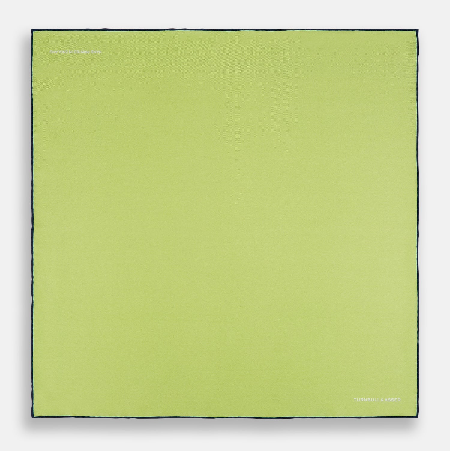 View 4 of product The Pistachio Green and Navy Piped Silk Pocket Square by Turnbull & Asser features crisp navy edging and an elegant brand logo, making it a refined addition to any formal outfit.