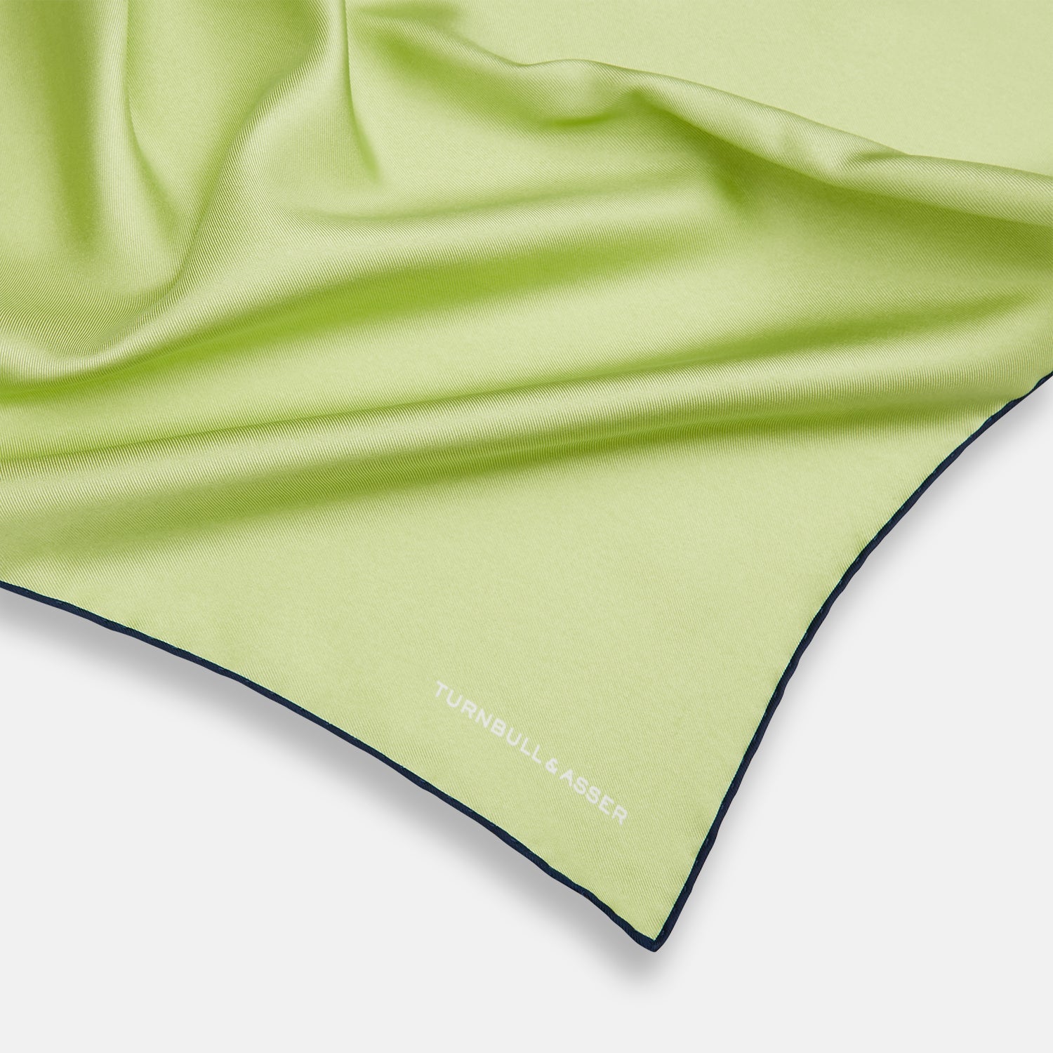View 2 of product The Pistachio Green and Navy Piped Silk Pocket Square by Turnbull & Asser features crisp navy edging and an elegant brand logo, making it a refined addition to any formal outfit.