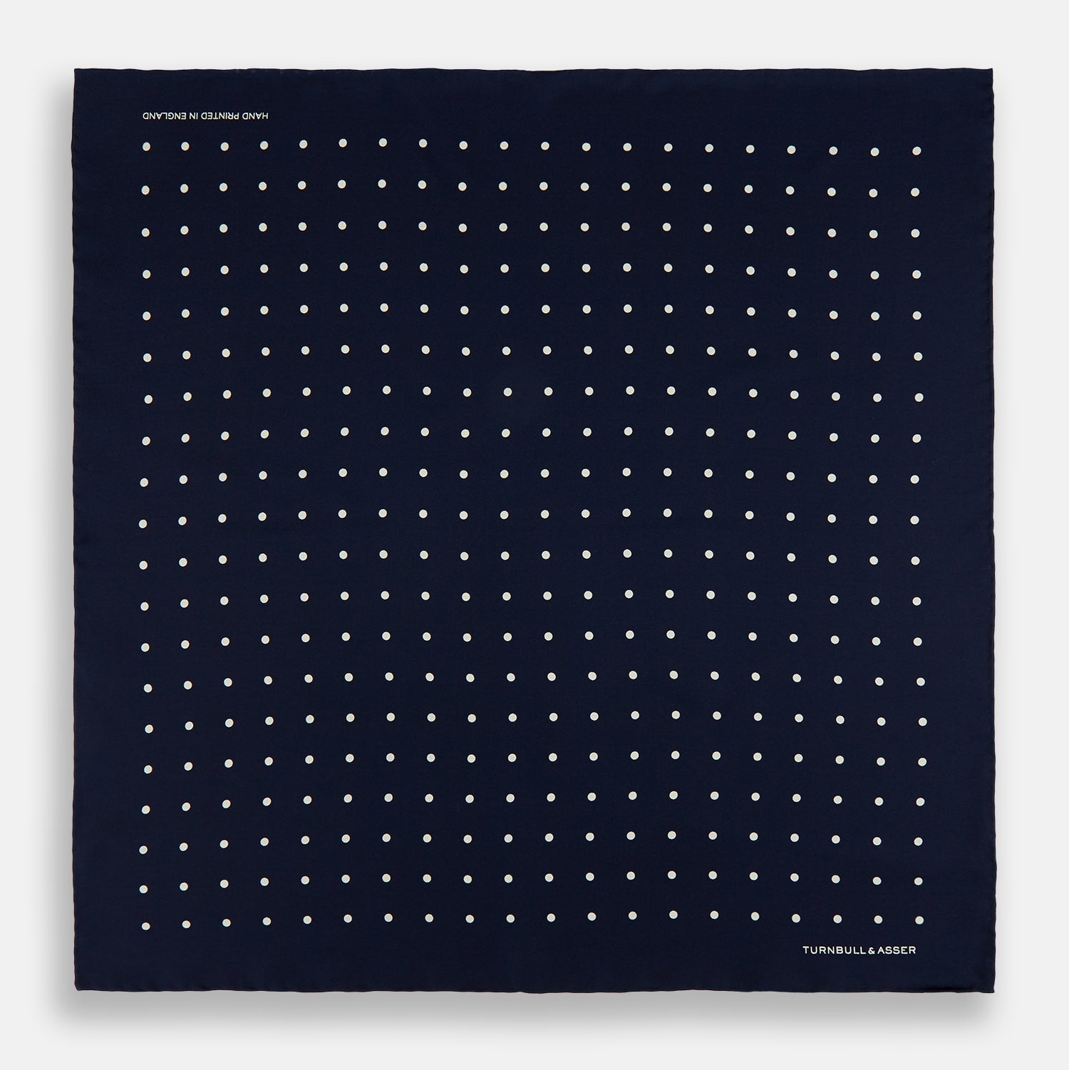 View 4 of product The Turnbull & Asser Navy and White Spot Silk Pocket Square features evenly spaced white polka dots and the brand logo in one corner—a stylish finishing touch for formal looks. One corner is neatly folded over.