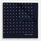 The Turnbull & Asser Navy and White Spot Silk Pocket Square features evenly spaced white polka dots and the brand logo in one corner—a stylish finishing touch for formal looks. One corner is neatly folded over.