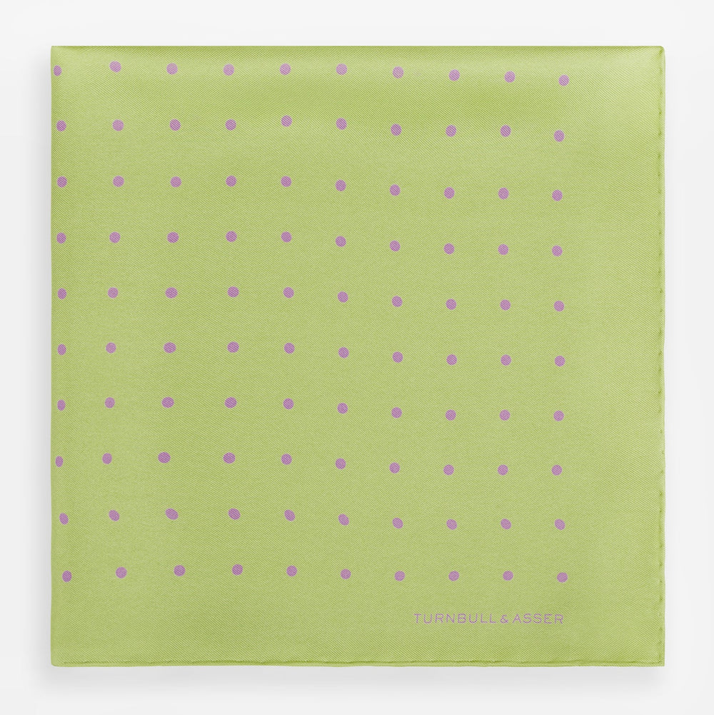 The Turnbull & Asser Melon Green and Lilac Spot Silk Pocket Square features evenly spaced lilac dots and the brand's name in one corner—a refined accessory for formal attire.