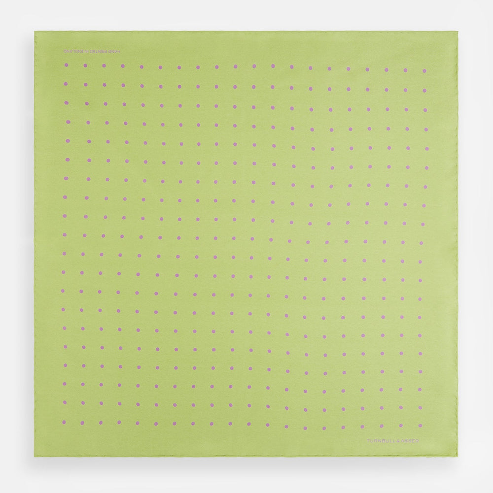 The Turnbull & Asser Melon Green and Lilac Spot Silk Pocket Square features evenly spaced lilac dots and the brand's name in one corner—a refined accessory for formal attire.
