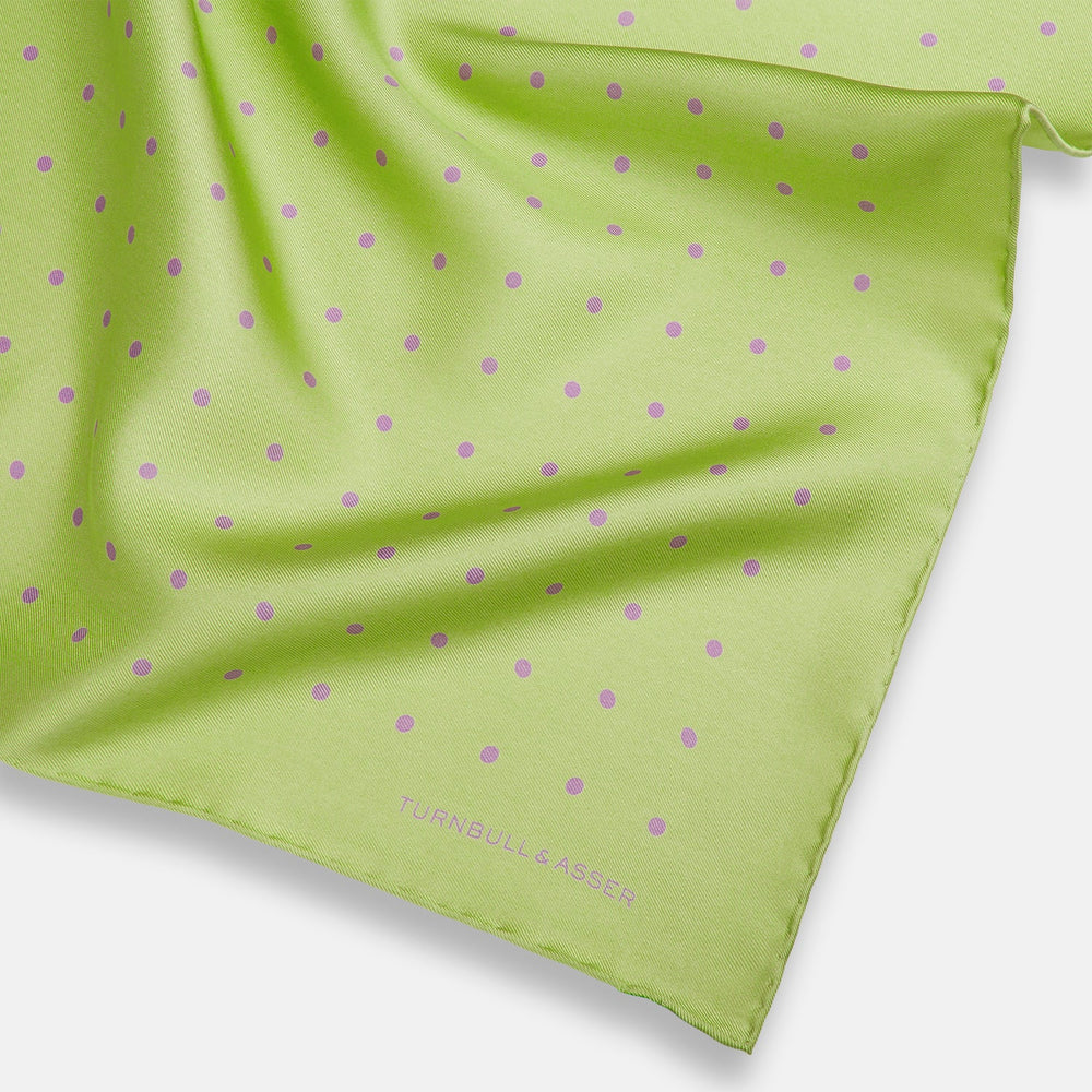 The Turnbull & Asser Melon Green and Lilac Spot Silk Pocket Square features evenly spaced lilac dots and the brand's name in one corner—a refined accessory for formal attire.