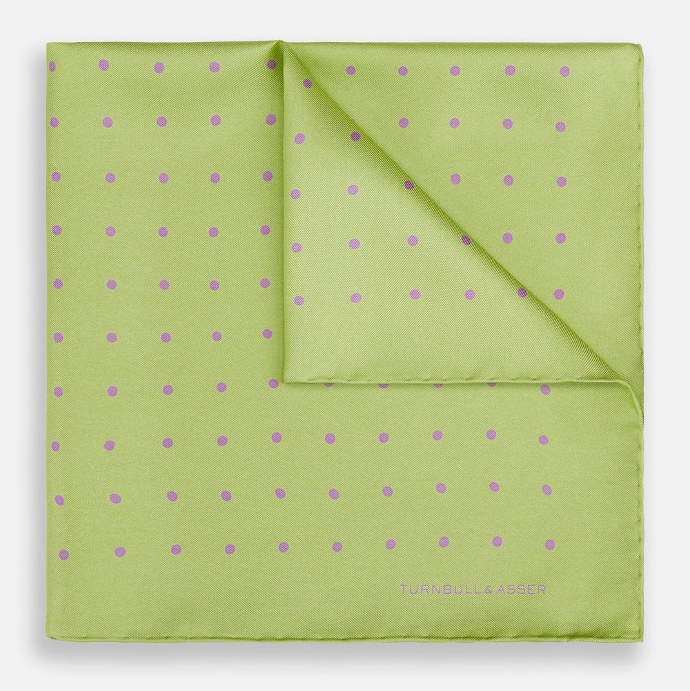 The Turnbull & Asser Melon Green and Lilac Spot Silk Pocket Square features evenly spaced lilac dots and the brand's name in one corner—a refined accessory for formal attire.