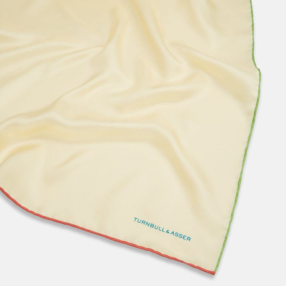 The Turnbull & Asser Ecru and Multicoloured Piped Silk Pocket Square features green and orange piping, blue "TURNBULL & ASSER" embroidery in the lower right, and a folded corner—a refined accessory for formal wear.