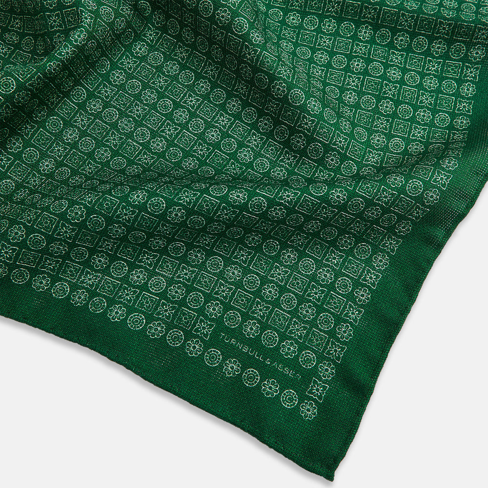 The Rosette Green Pocket Square in Silk by Turnbull & Asser UK features a small geometric medallion pattern and is shown folded to display a contrasting fine black-and-white design on the reverse side.