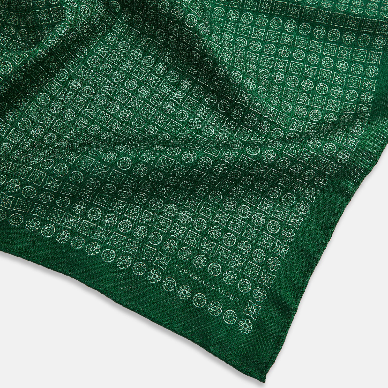 View 4 of product The Rosette Green Pocket Square in Silk by Turnbull & Asser UK features a small geometric medallion pattern and is shown folded to display a contrasting fine black-and-white design on the reverse side.