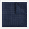 View 2 of product The Checked Blue Pocket Square in Silk by Turnbull & Asser UK features a navy base with a light blue grid pattern on one side and a refined dotted design on the other. This double-sided accessory is shown partially folded to elegantly showcase both distinctive patterns.