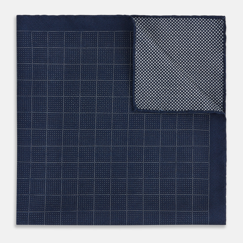 The Checked Blue Pocket Square in Silk by Turnbull & Asser UK features a navy base with a light blue grid pattern on one side and a refined dotted design on the other. This double-sided accessory is shown partially folded to elegantly showcase both distinctive patterns.
