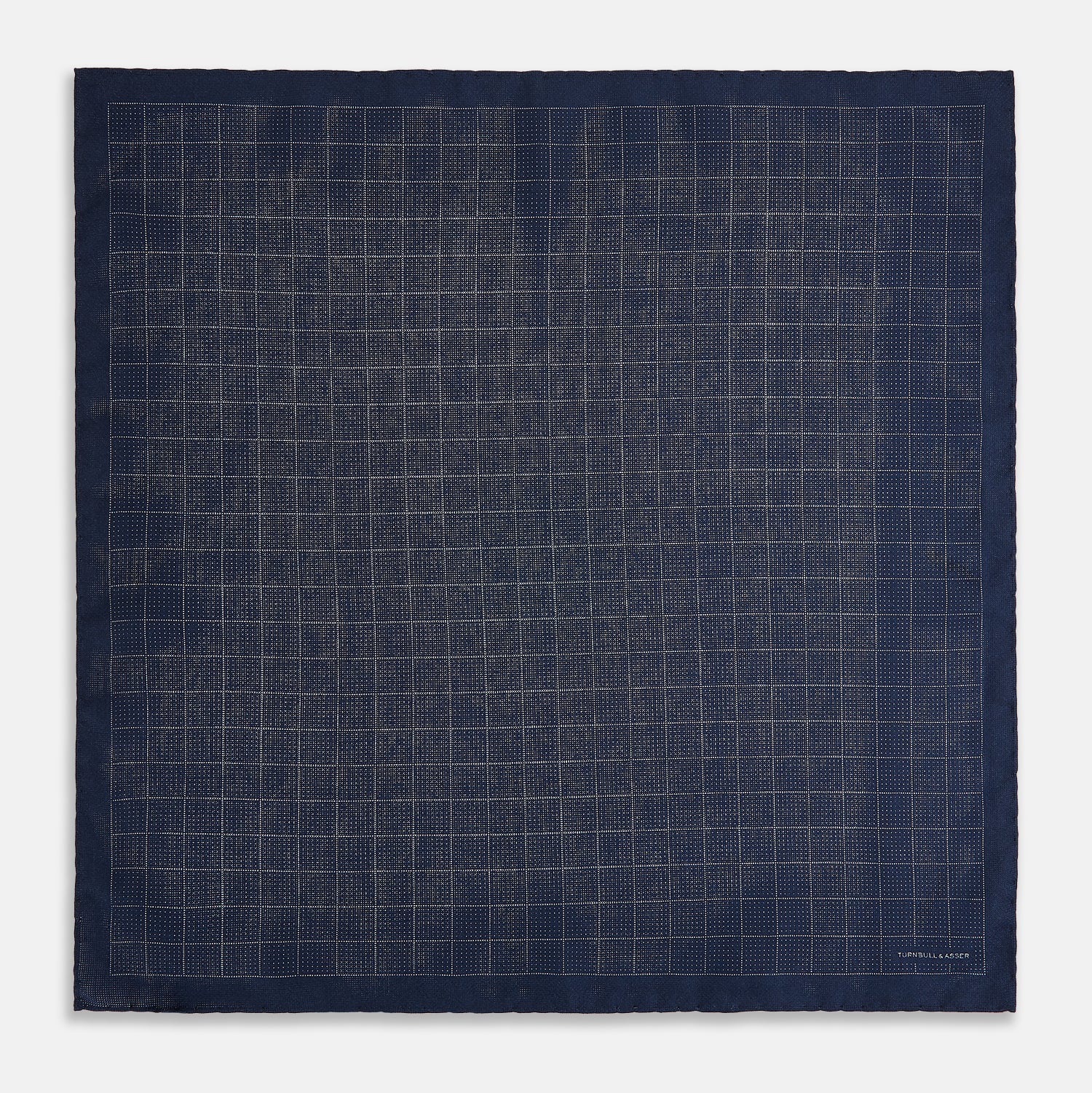 View 5 of product The Checked Blue Pocket Square in Silk by Turnbull & Asser UK features a navy base with a light blue grid pattern on one side and a refined dotted design on the other. This double-sided accessory is shown partially folded to elegantly showcase both distinctive patterns.