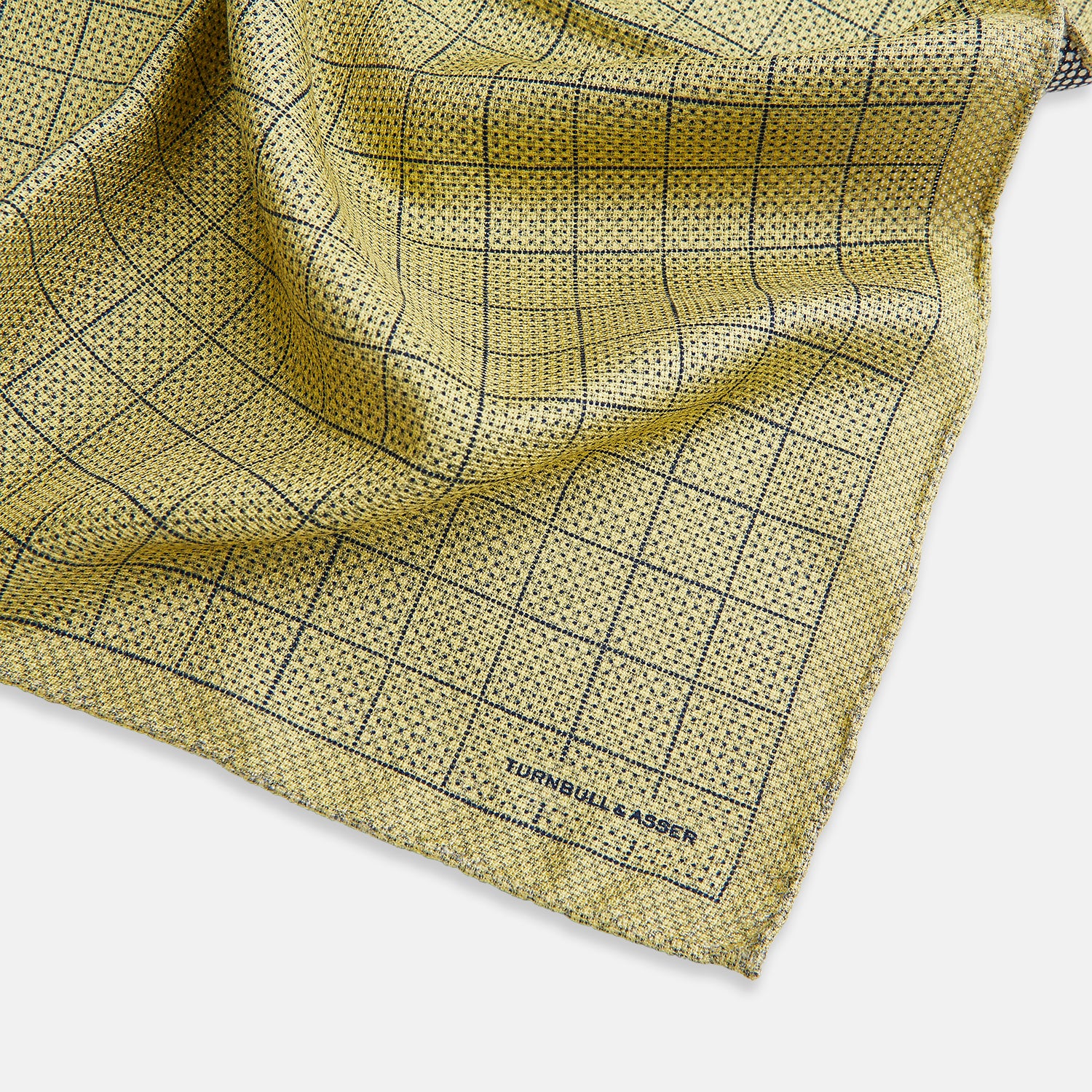 View 2 of product A yellow silk pocket square featuring a small black grid pattern of dotted squares, neatly folded at one corner. "Turnbull & Asser UK" is printed in the bottom right corner.