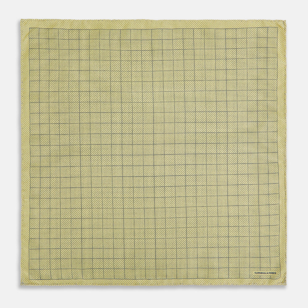 A yellow silk pocket square featuring a small black grid pattern of dotted squares, neatly folded at one corner. "Turnbull & Asser UK" is printed in the bottom right corner.