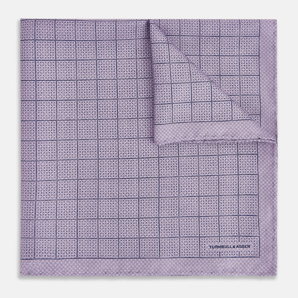 The Checked Lilac Pocket Square in Silk by Turnbull & Asser UK features a grid pattern in purple with a solid border, neatly folded to display its double-sided design and contrasting black and white dotted squares on the reverse side.